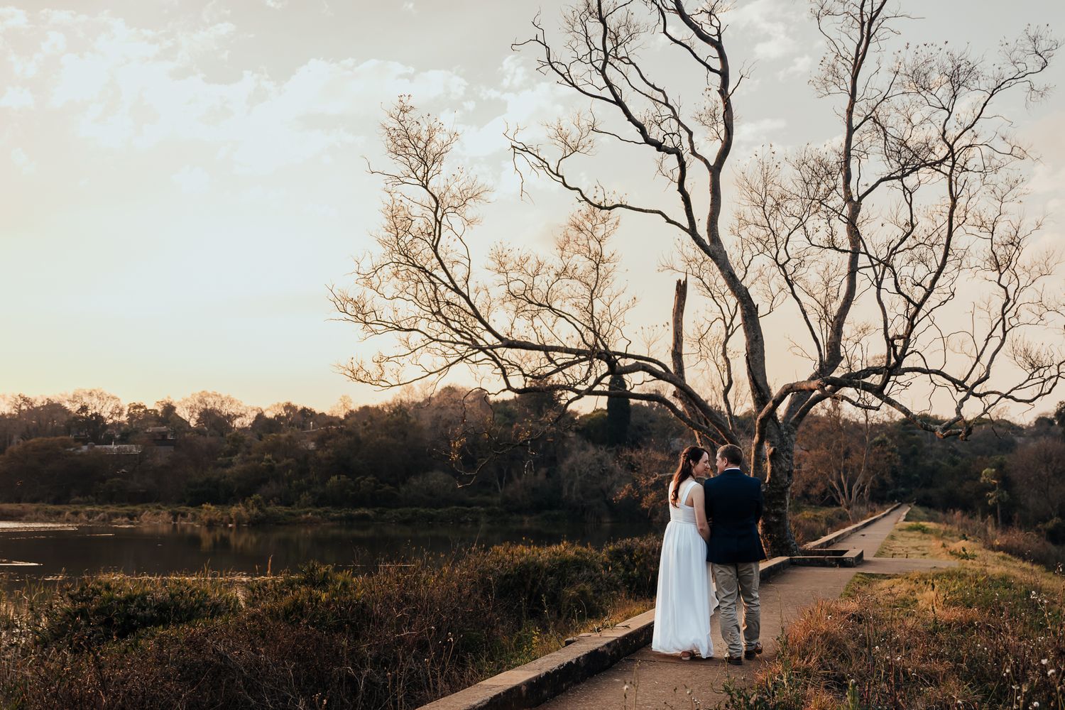Wide panoramic view of couple on dirt path with bare trees at sunset.