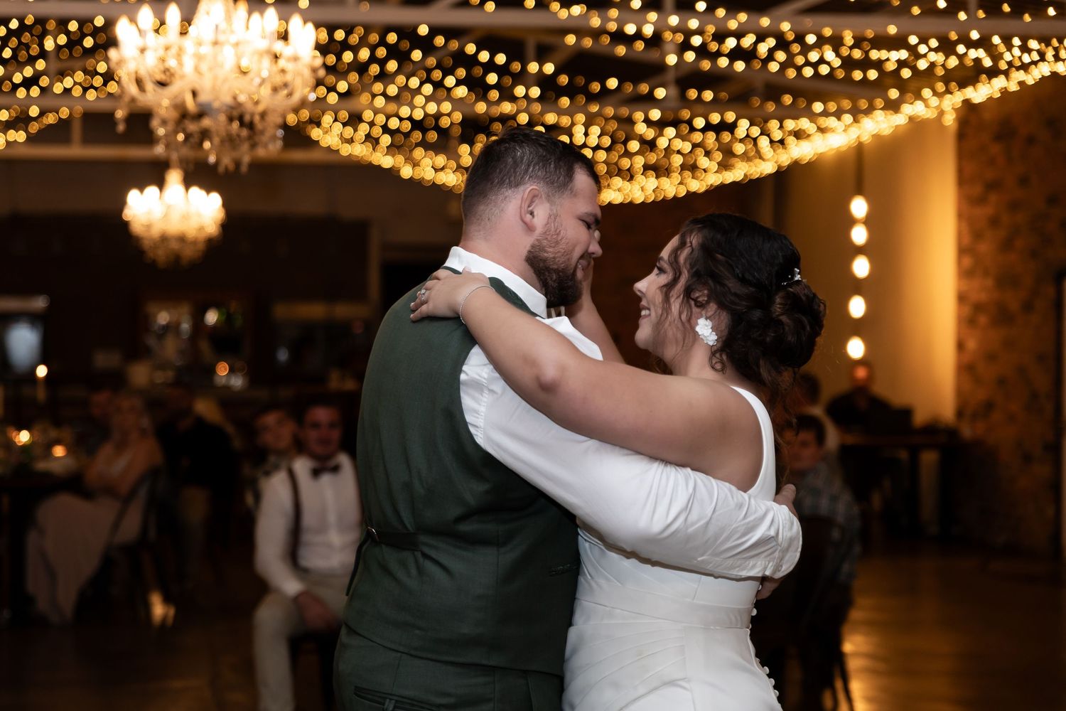A romantic embrace during a wedding dance beneath twinkling fairy lights and chandeliers.