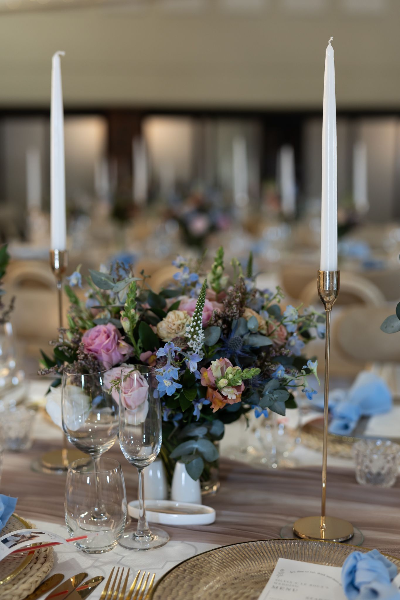Romantic table decor featuring blue and pink floral arrangements with gold taper candle holders.