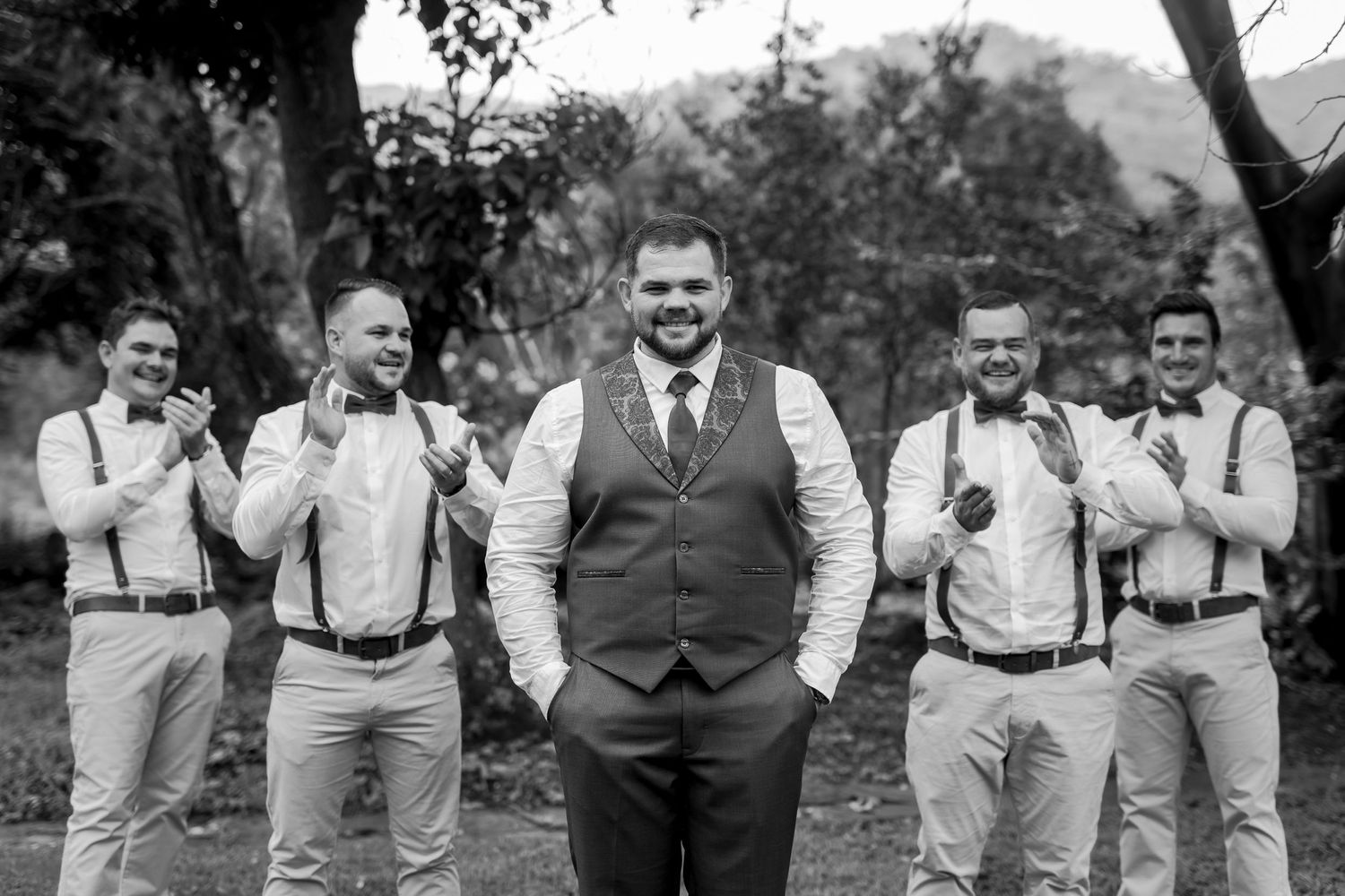 Wedding party in formal attire poses outdoors with coordinated black and white outfits.