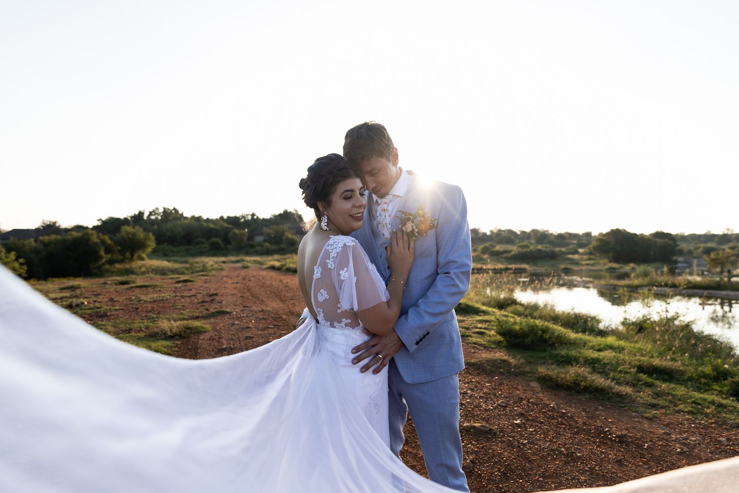 A romantic wedding photo with flowing white dress against a natural landscape.