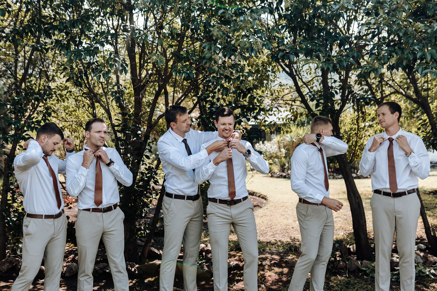 Group of groomsmen in light colored suits and red ties having fun outdoors.