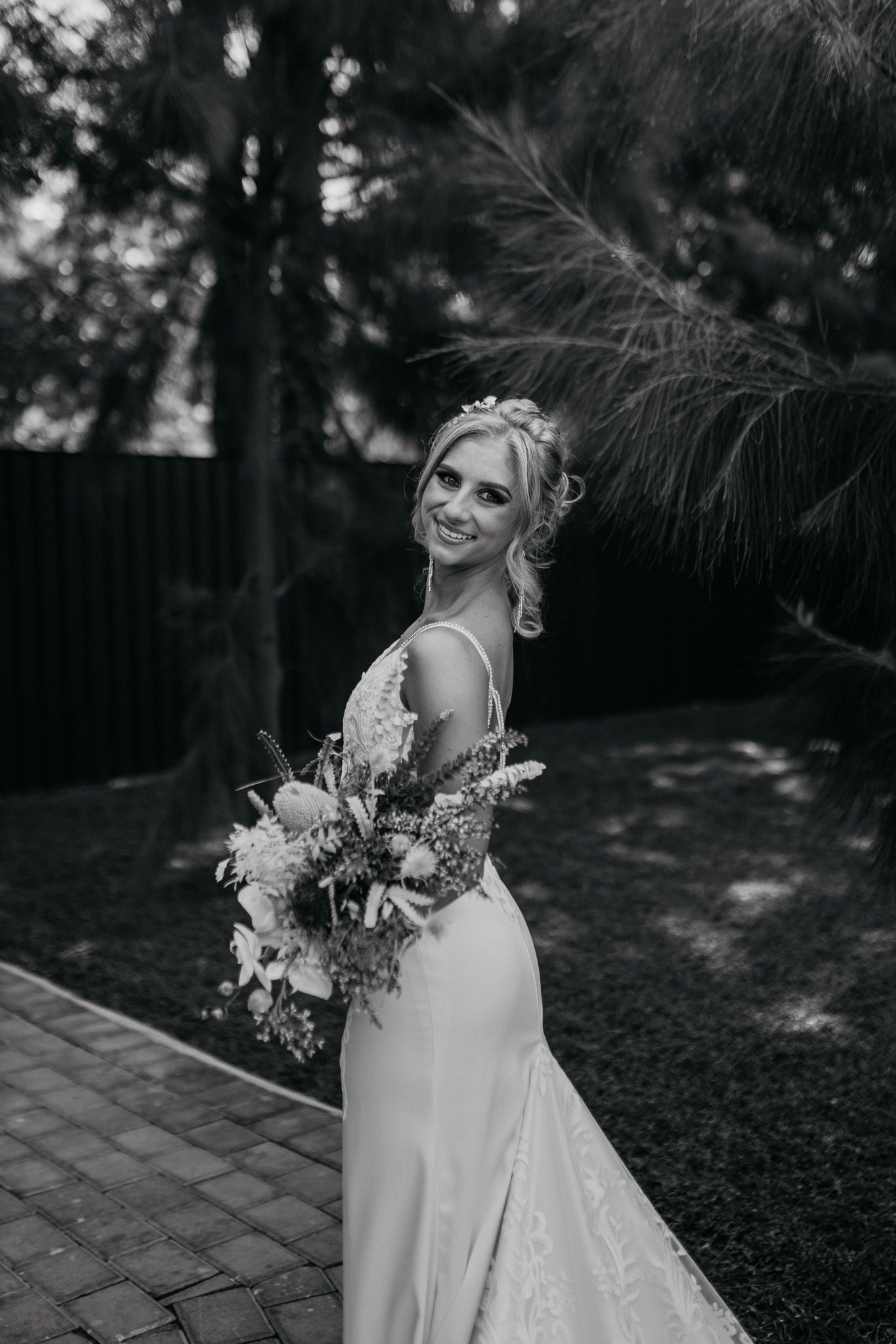 Black and white portrait of bride with bouquet on outdoor brick pathway.