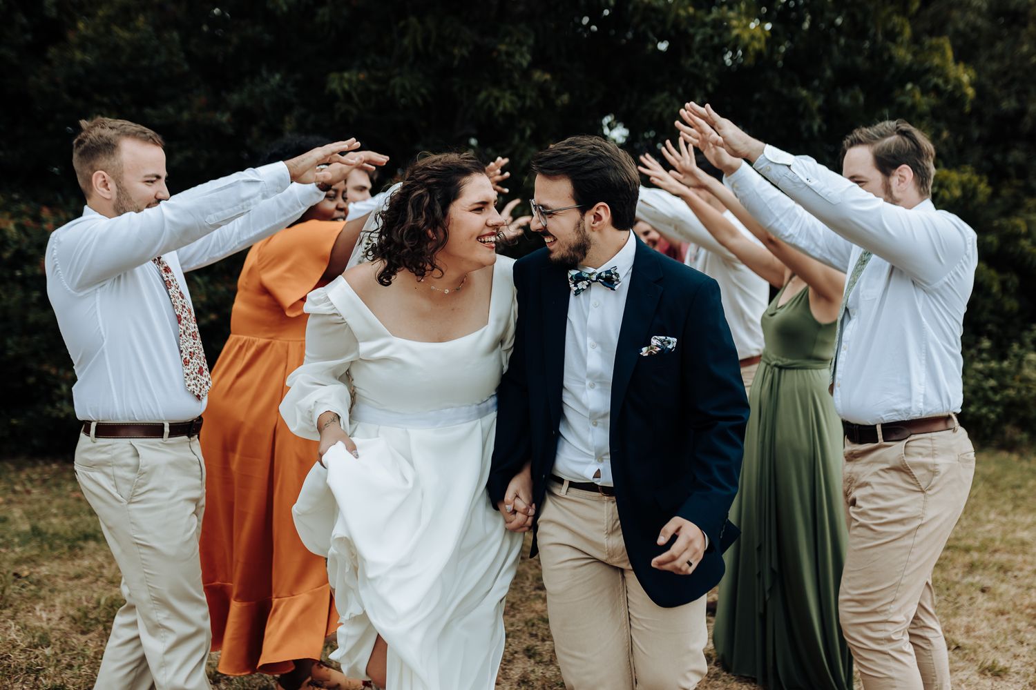 Wedding party forms arch with raised arms while couple walks underneath.