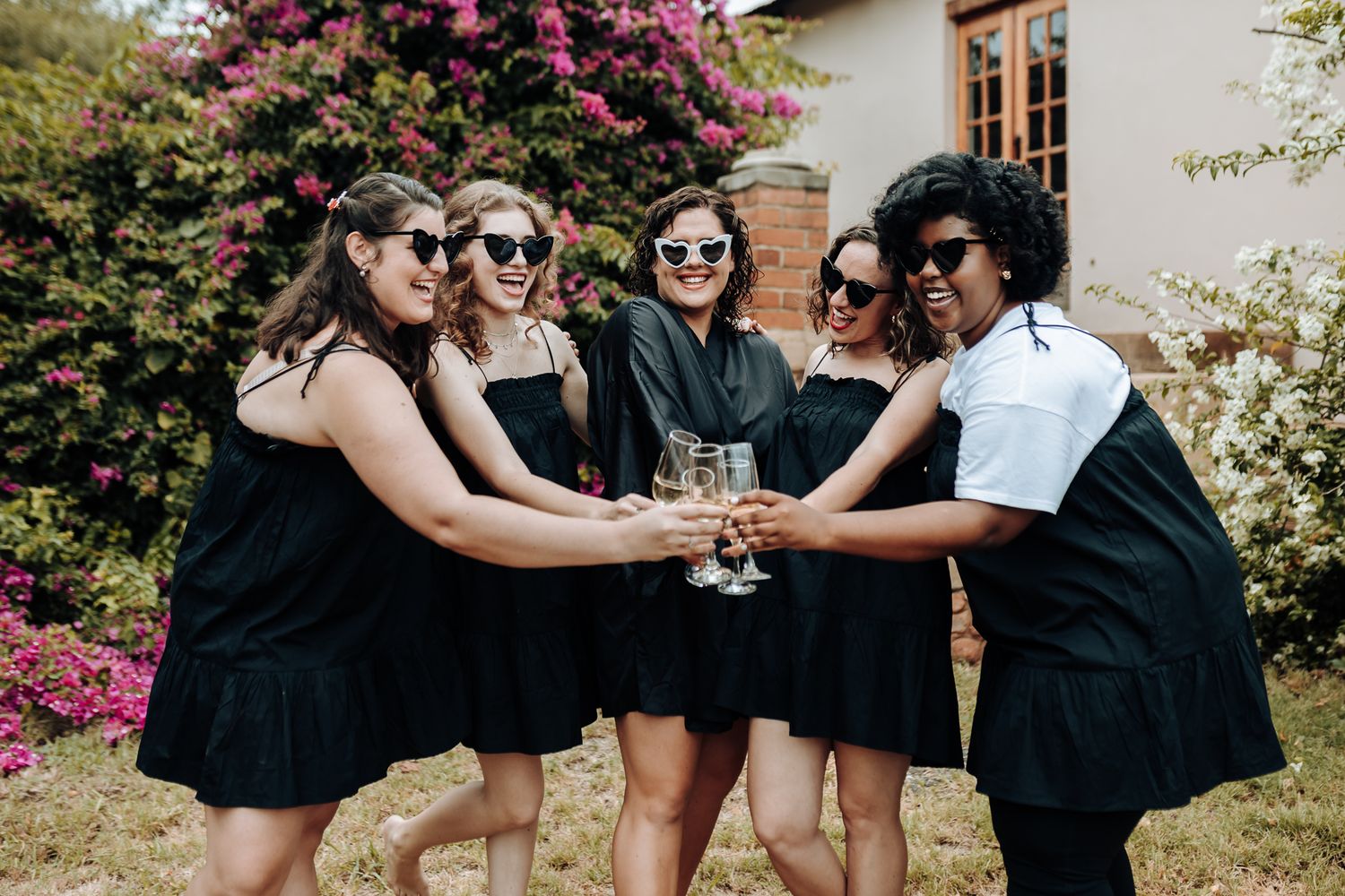 Wedding party in black dresses joining hands in a circle outdoors.
