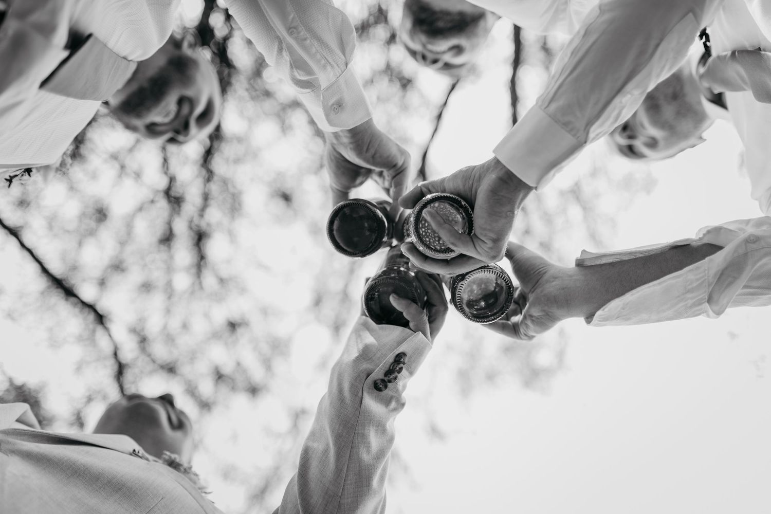 Black and white overhead view of four champagne glasses clinking together in celebration.