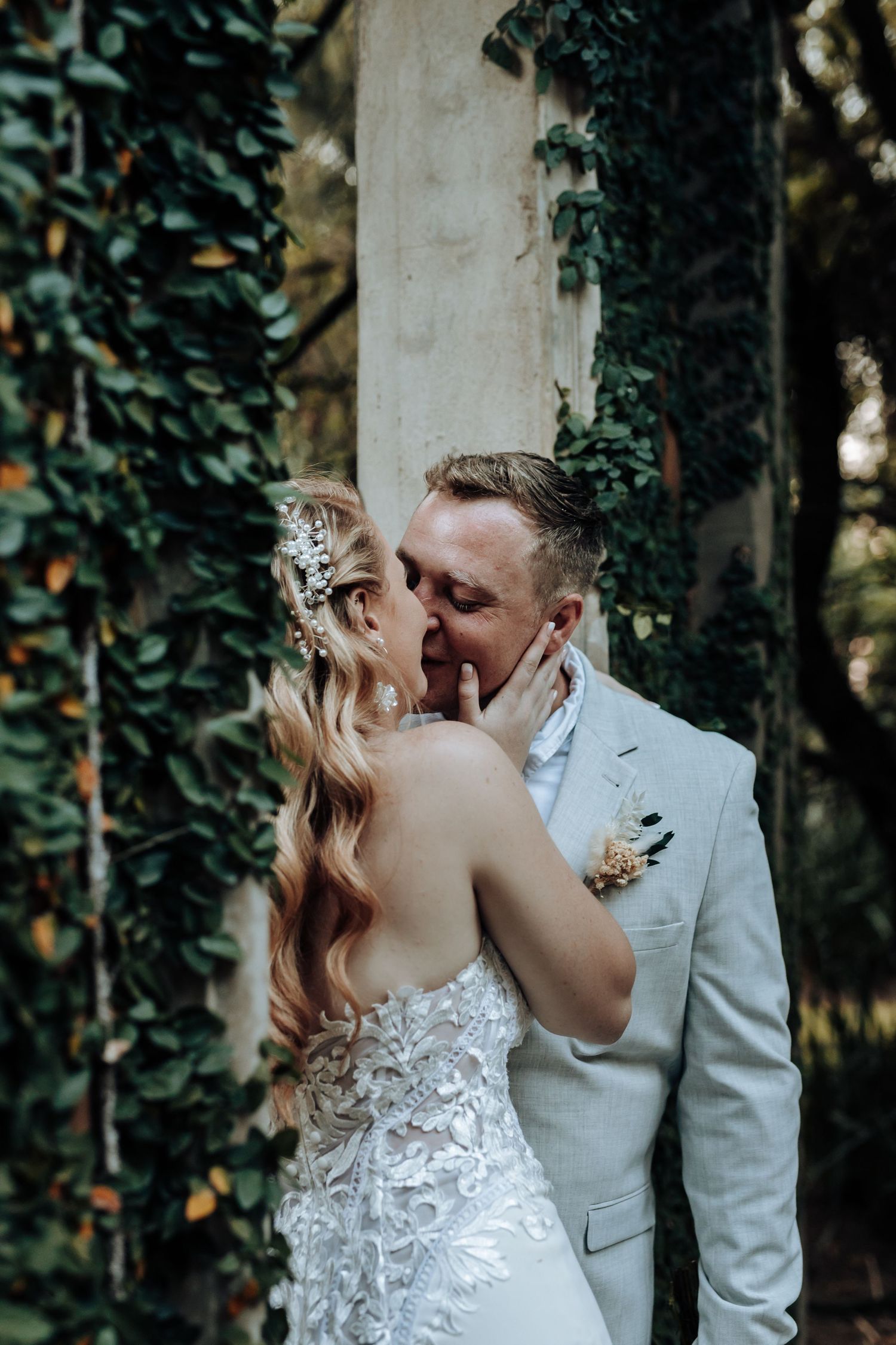An intimate wedding moment captured against a backdrop of lush green ivy and white columns.