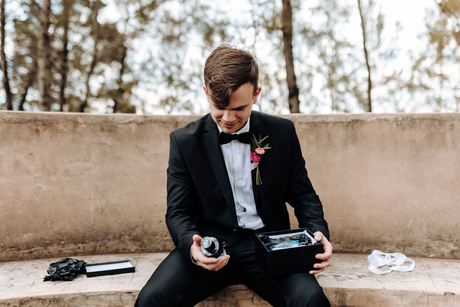 A person in formal attire sits on concrete bench checking their phone.