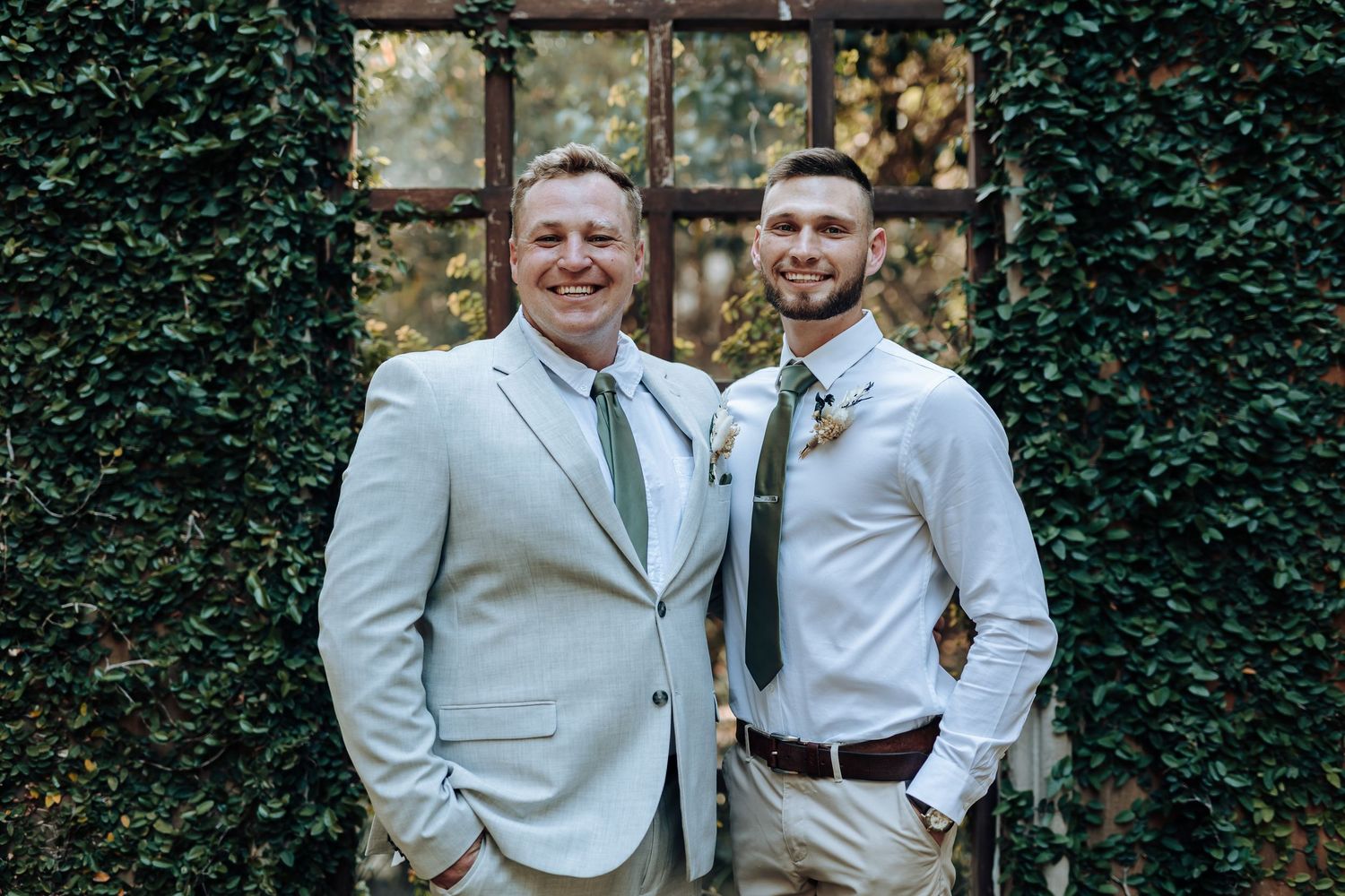 Two members of wedding party pose together against ivy-covered wall backdrop.