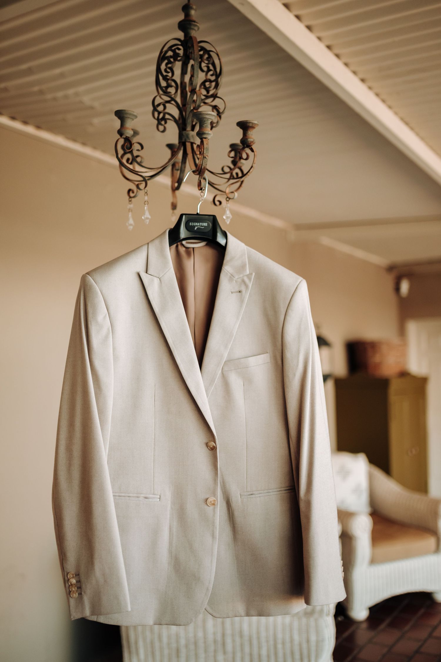 Light beige suit jacket hanging from ornate iron chandelier against white ceiling.