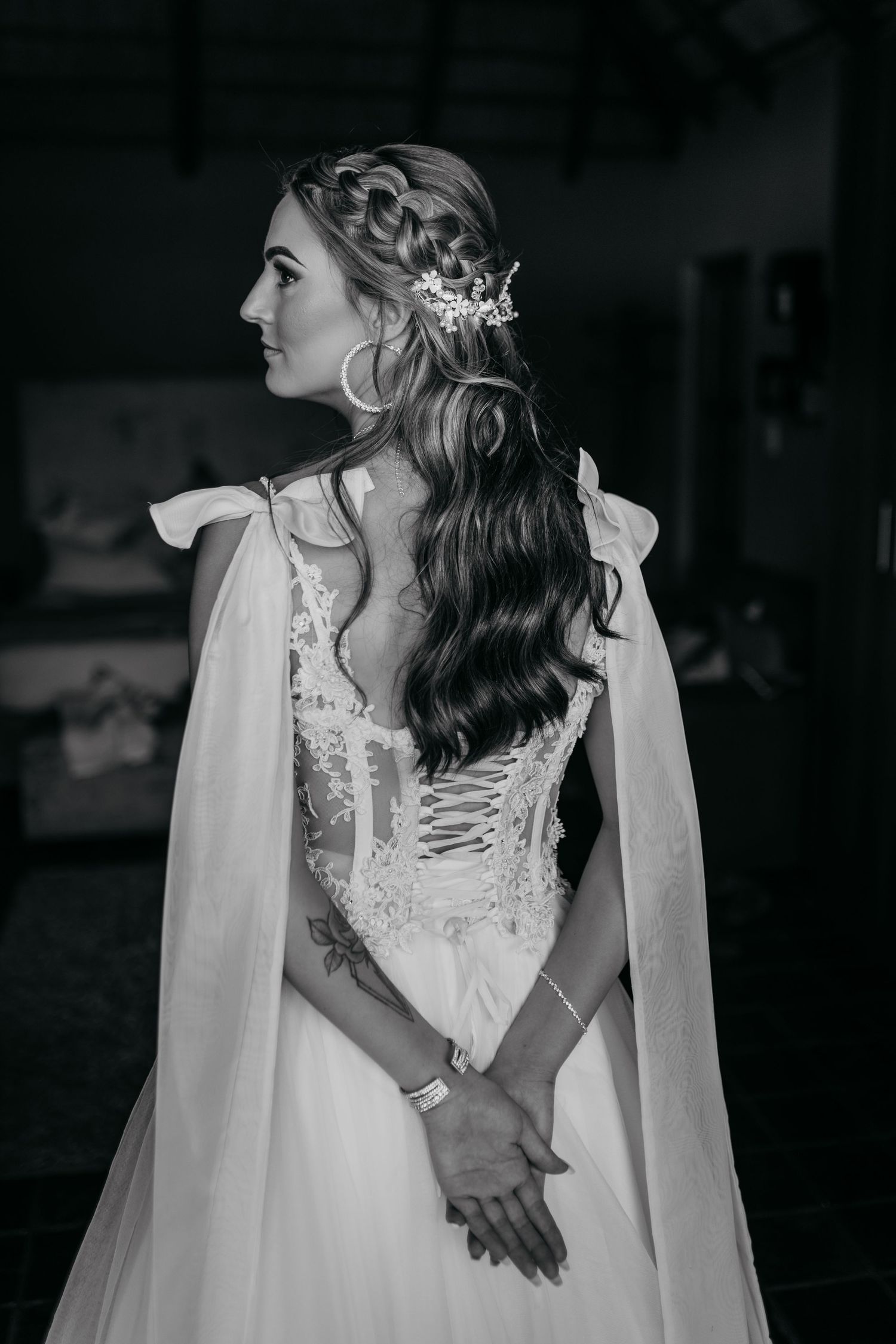 Side profile of a bridal hairstyle with braided crown and flowing waves against a dark background.