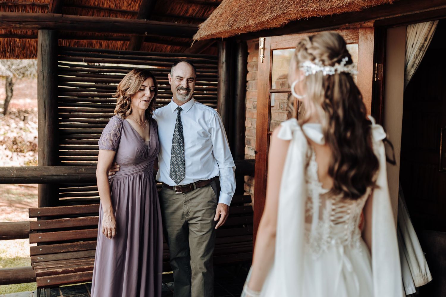 A bride in a white dress shares a moment with loved ones in a rustic wooden building setting.