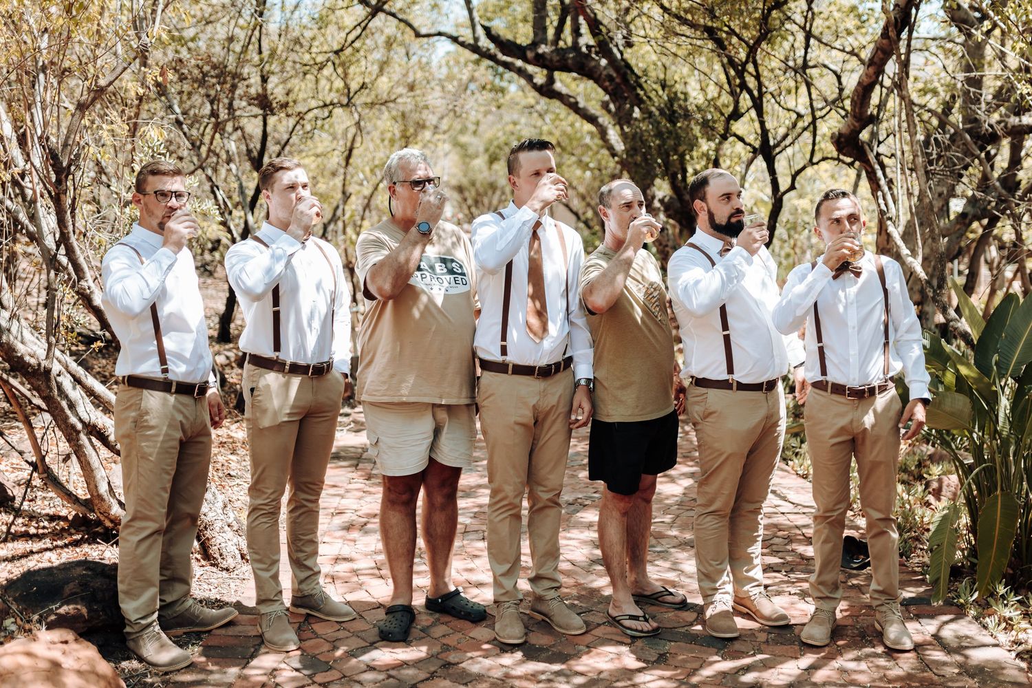 Wedding party in coordinated attire with white shirts and suspenders posed outdoors.