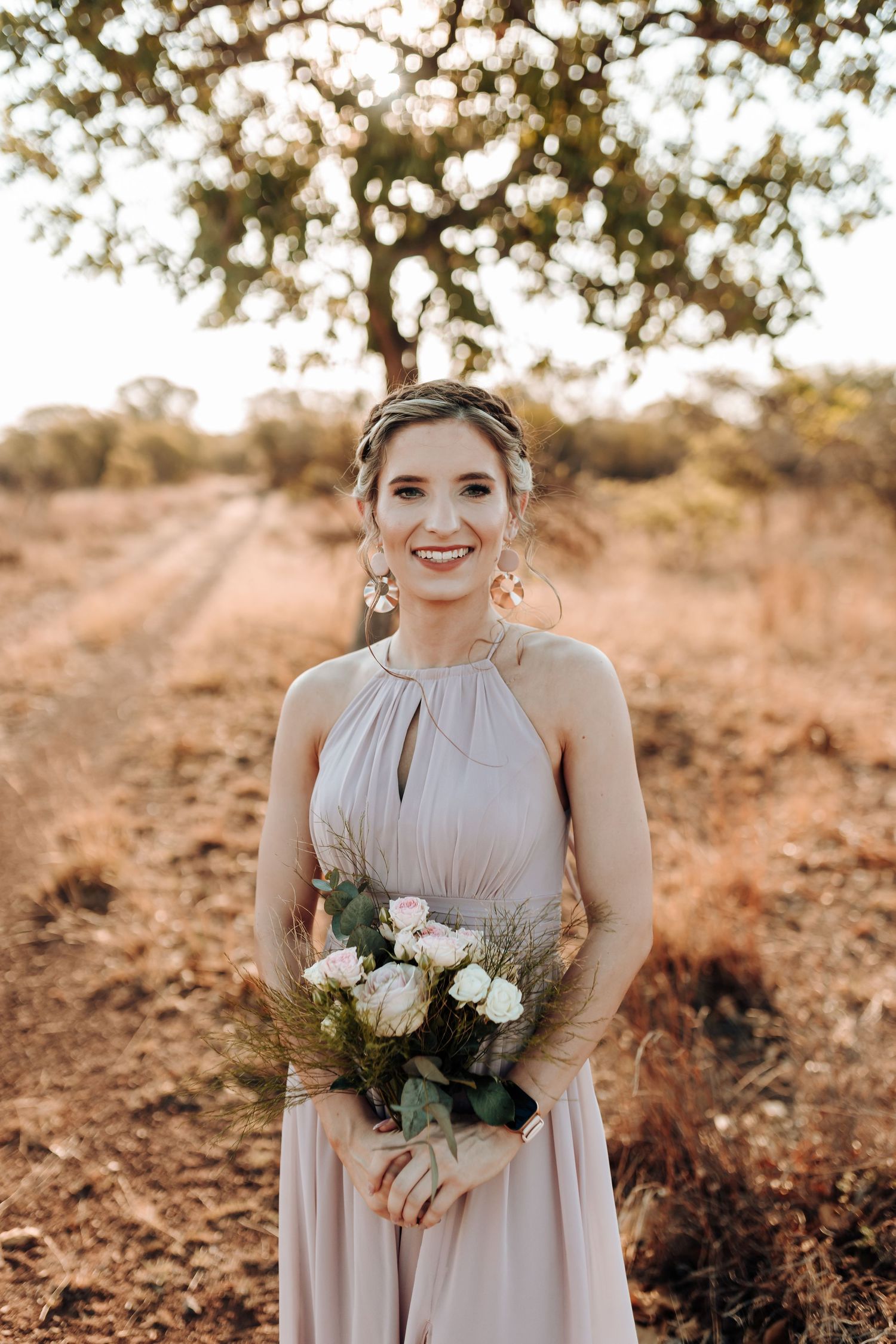 Wedding party member in halter dress holding white roses against warm outdoor background.