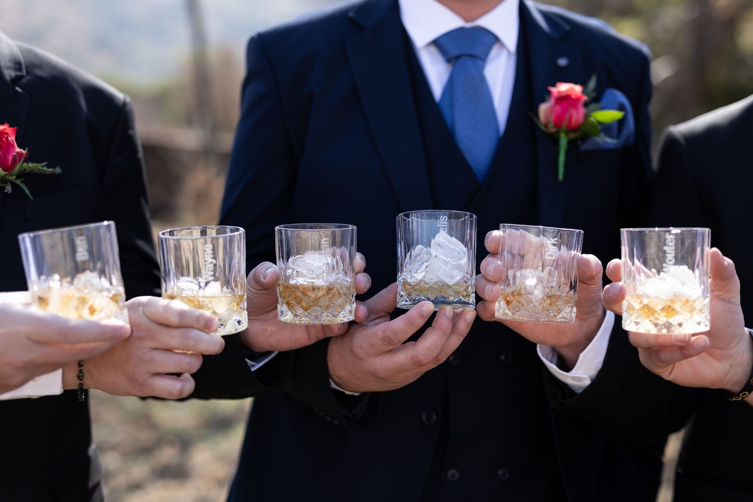 Hands holding elegant crystal whiskey glasses with cocktails during a formal wedding celebration.