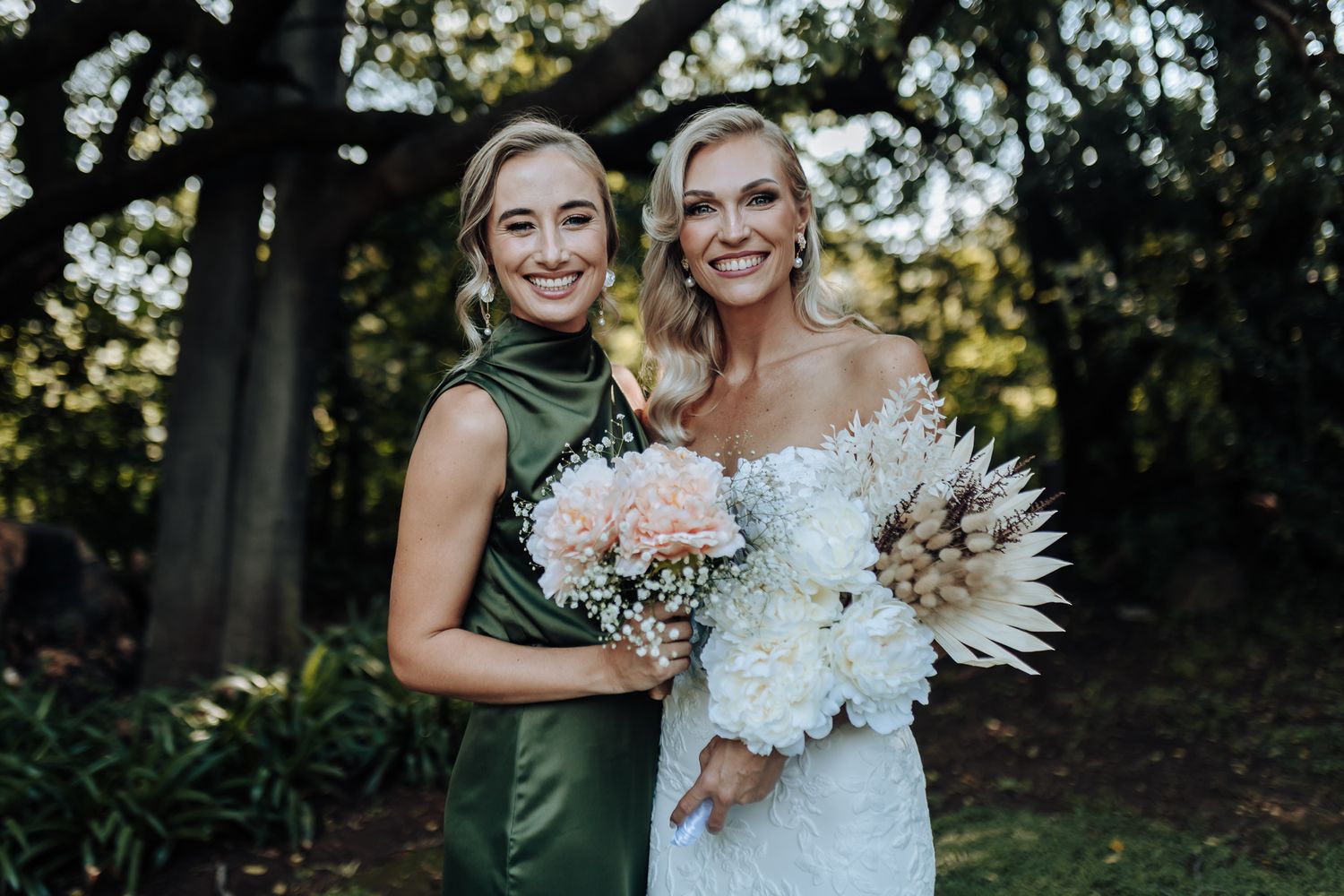 Outdoor wedding portrait featuring contrasting white lace and emerald green dresses with elegant floral bouquets.