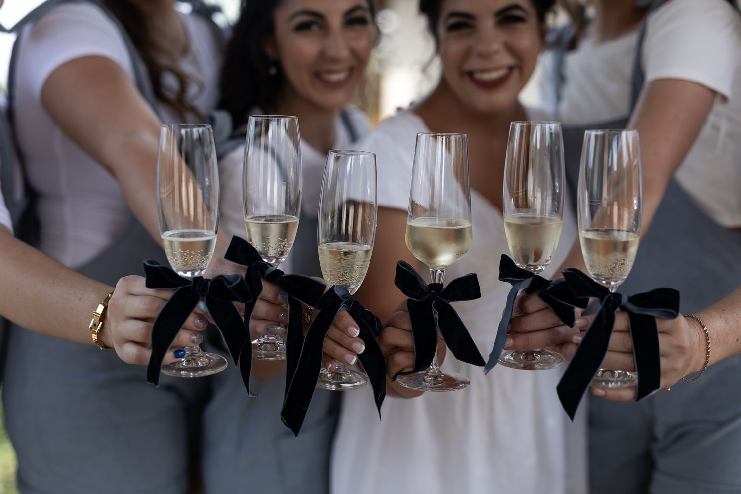 Champagne glasses decorated with black bows held by hands wearing coordinated outfits.