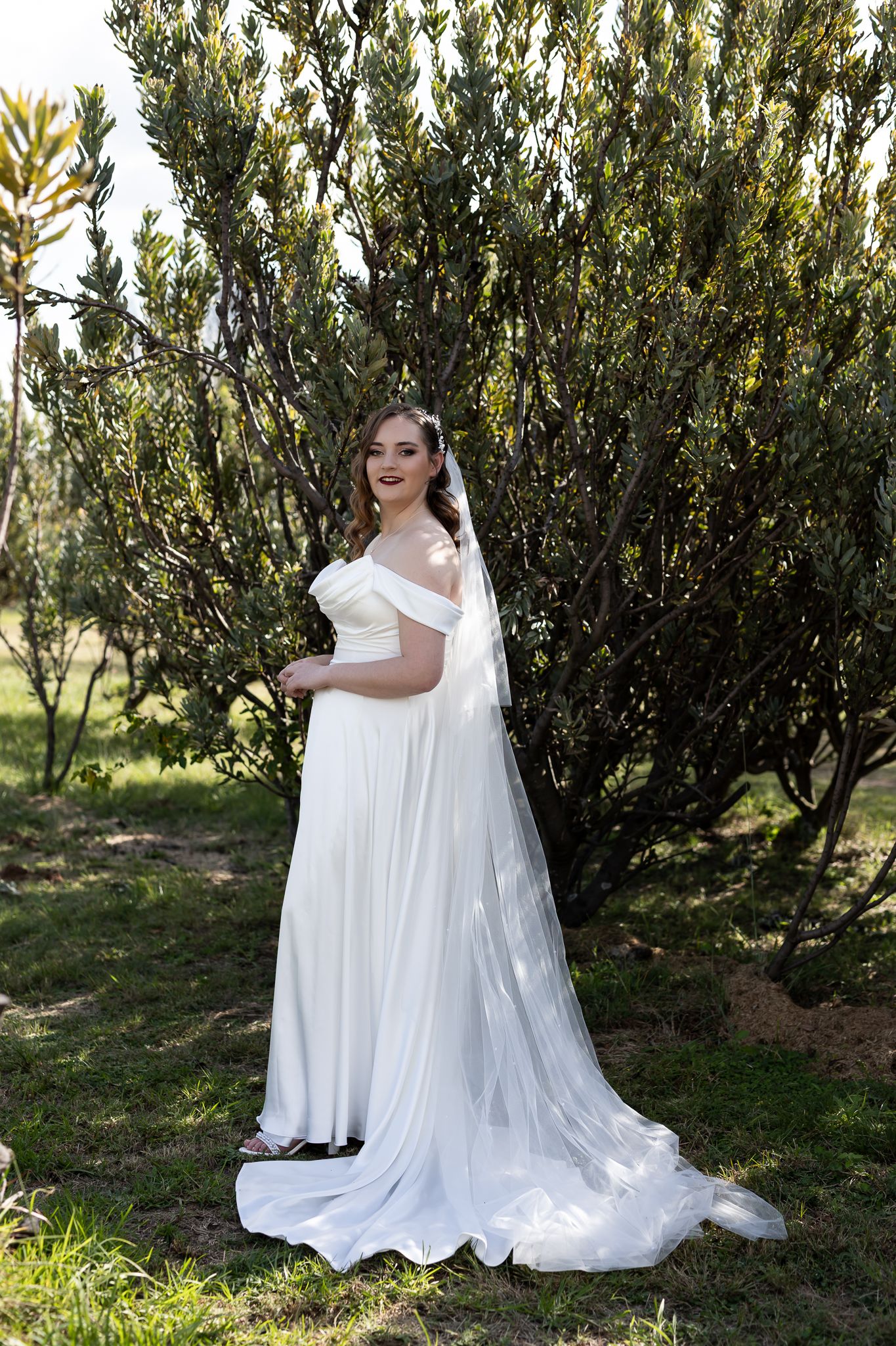 Elegant wedding dress with flowing train photographed against lush greenery in natural outdoor setting.