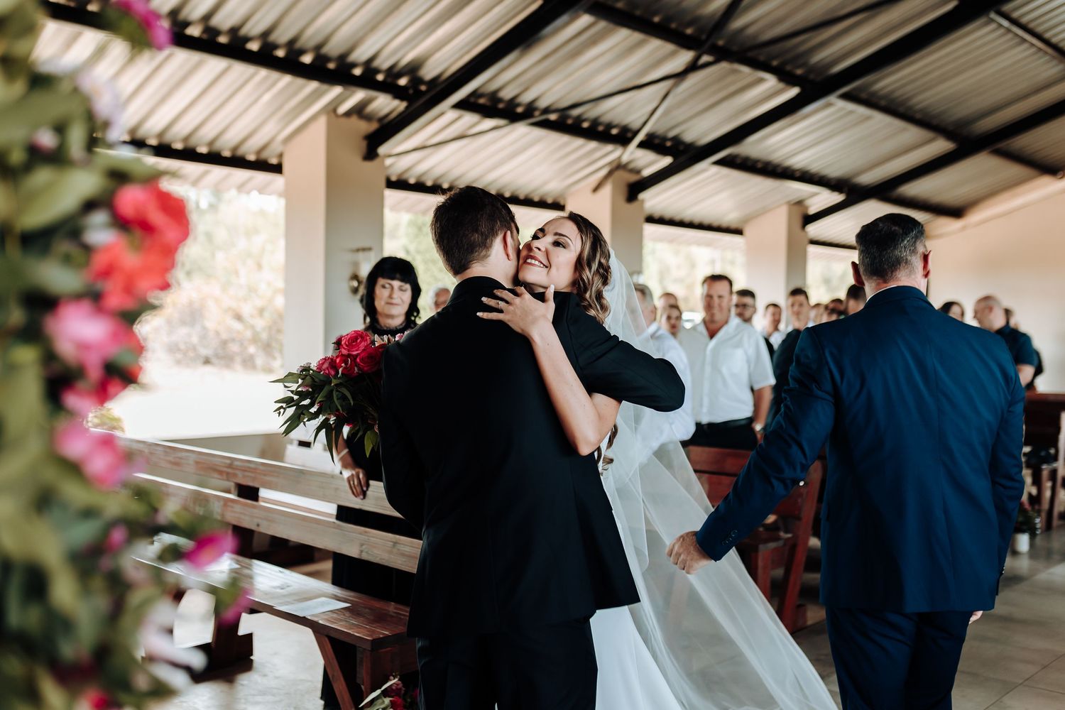 Intimate moment during wedding ceremony with floral decor and wooden benches.