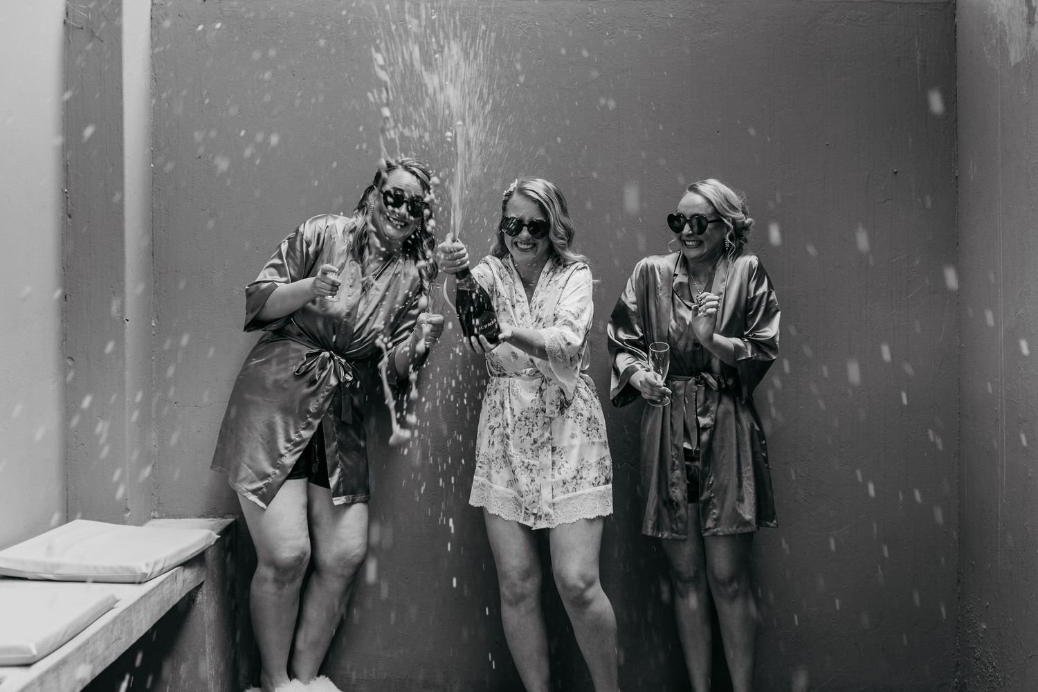 Black and white photo shows three friends celebrating with champagne spray.