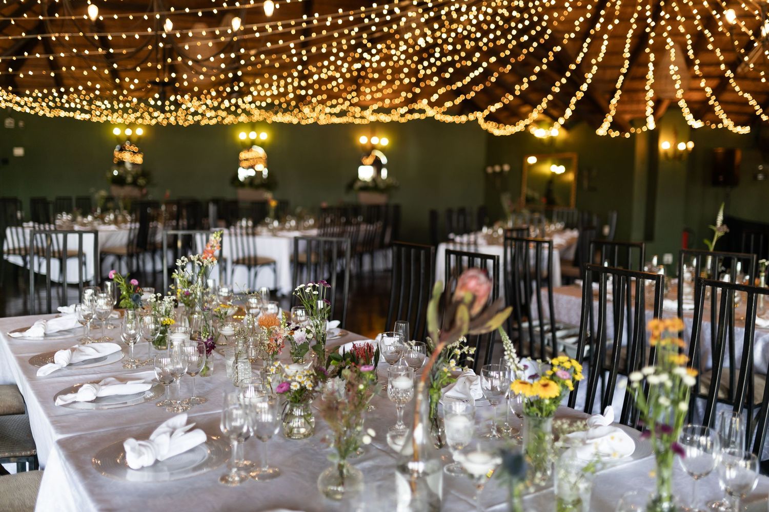Wedding reception tables set under stunning ceiling of twinkle lights.