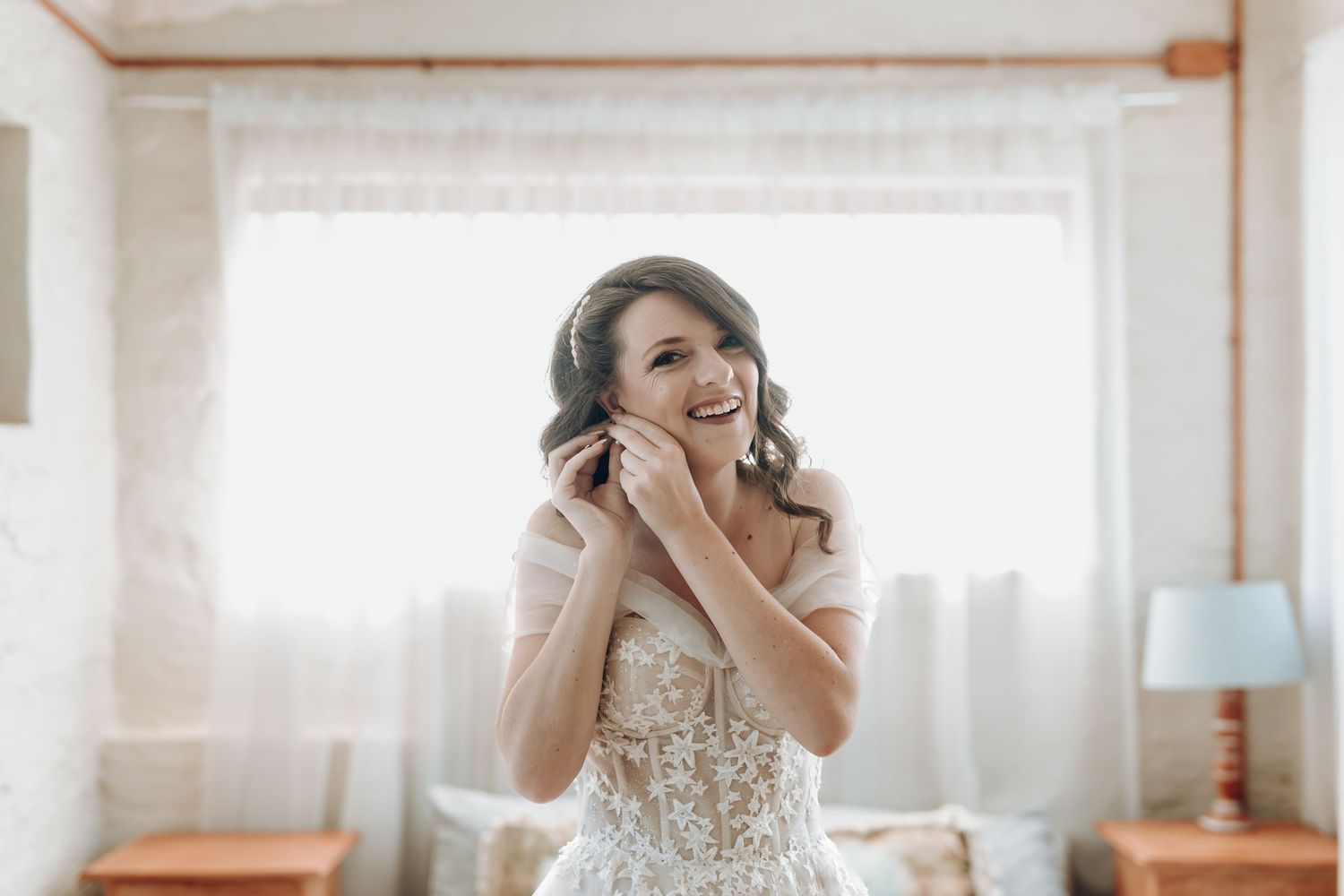 A joyful wedding morning scene with natural light streaming through sheer curtains.