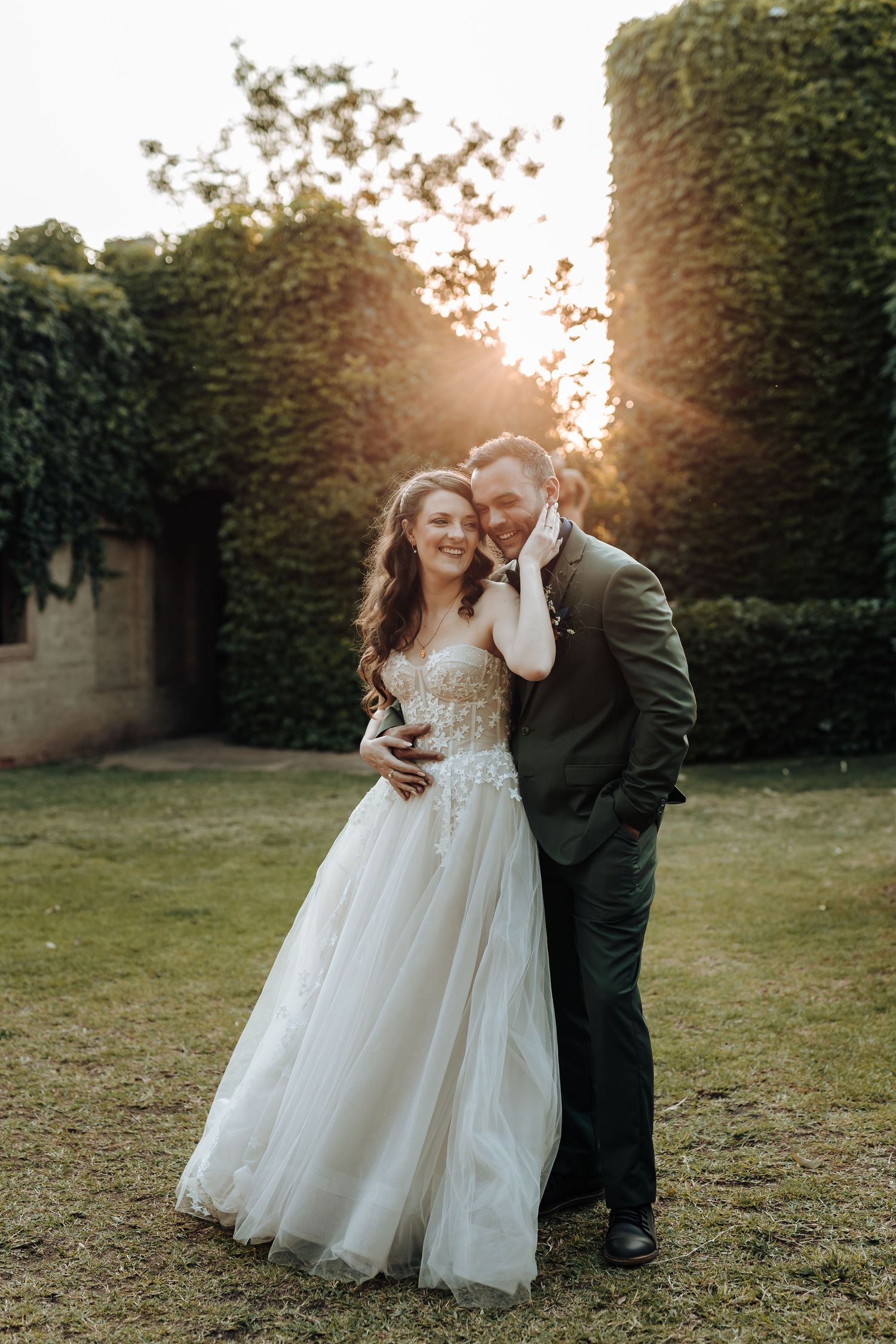 Romantic sunset portrait of newlyweds embracing in garden with ivy-covered walls.