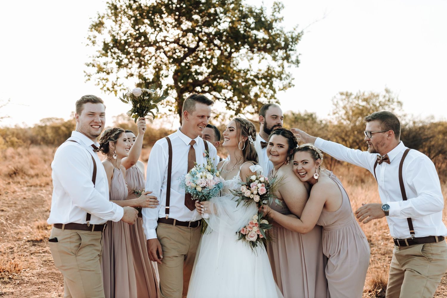 Wedding group shares intimate celebratory moment in natural outdoor setting.