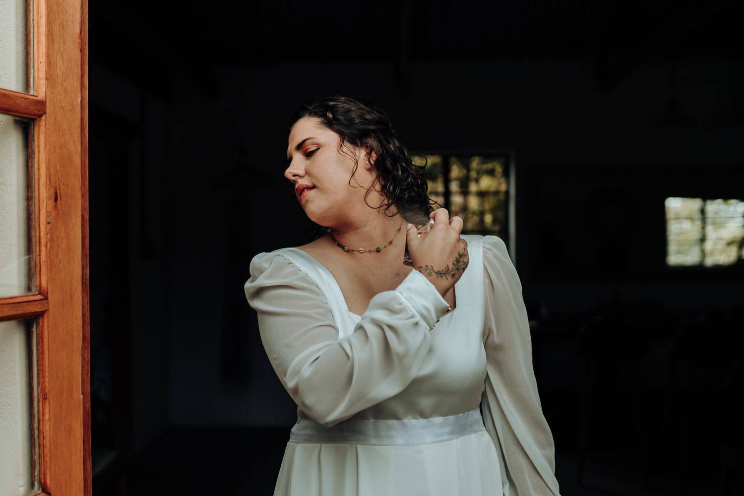Artistic portrait of a person in a white dress adjusting their necklace in natural window light.