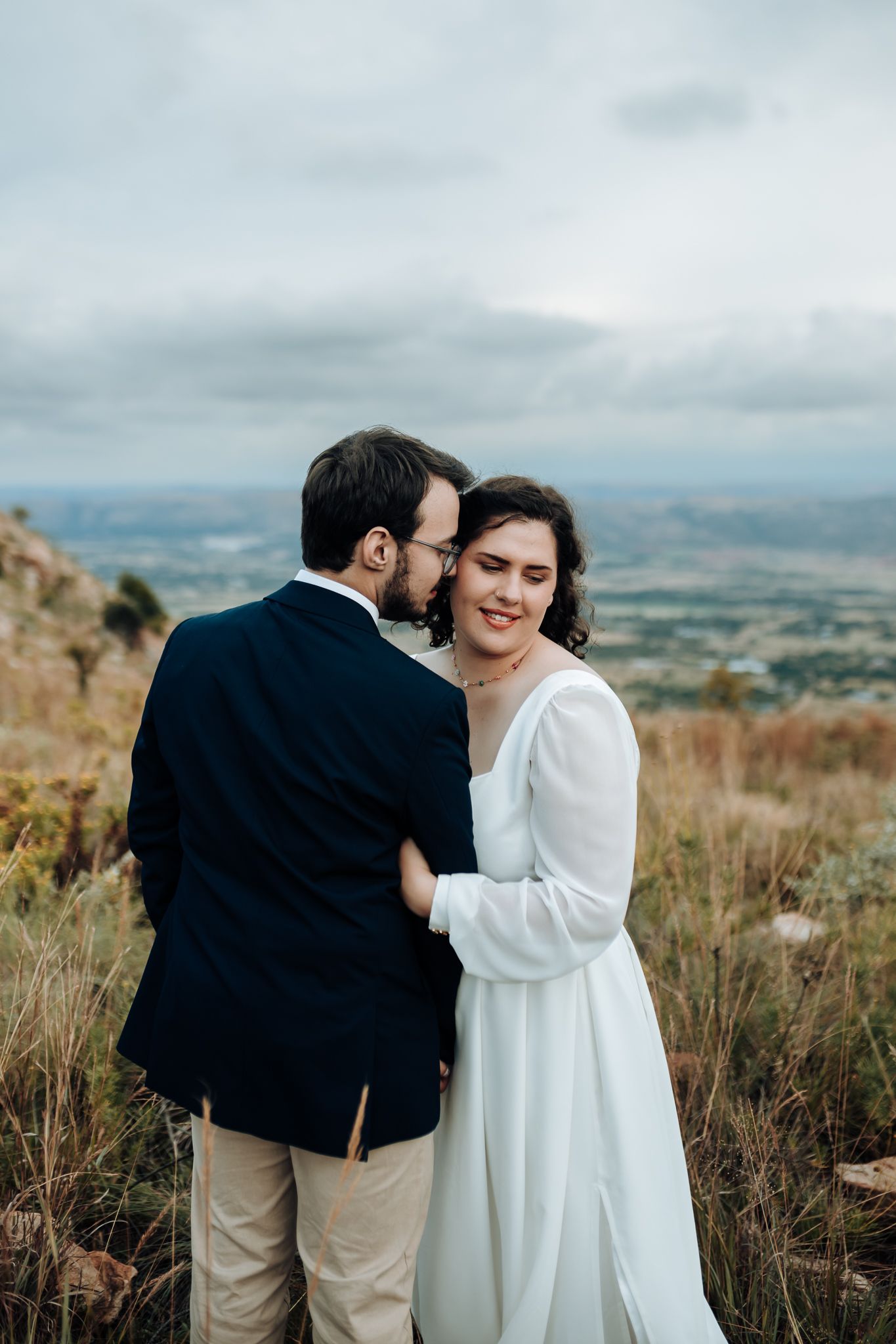 A sweet moment between newlyweds on a hilltop overlooking a vast valley landscape.