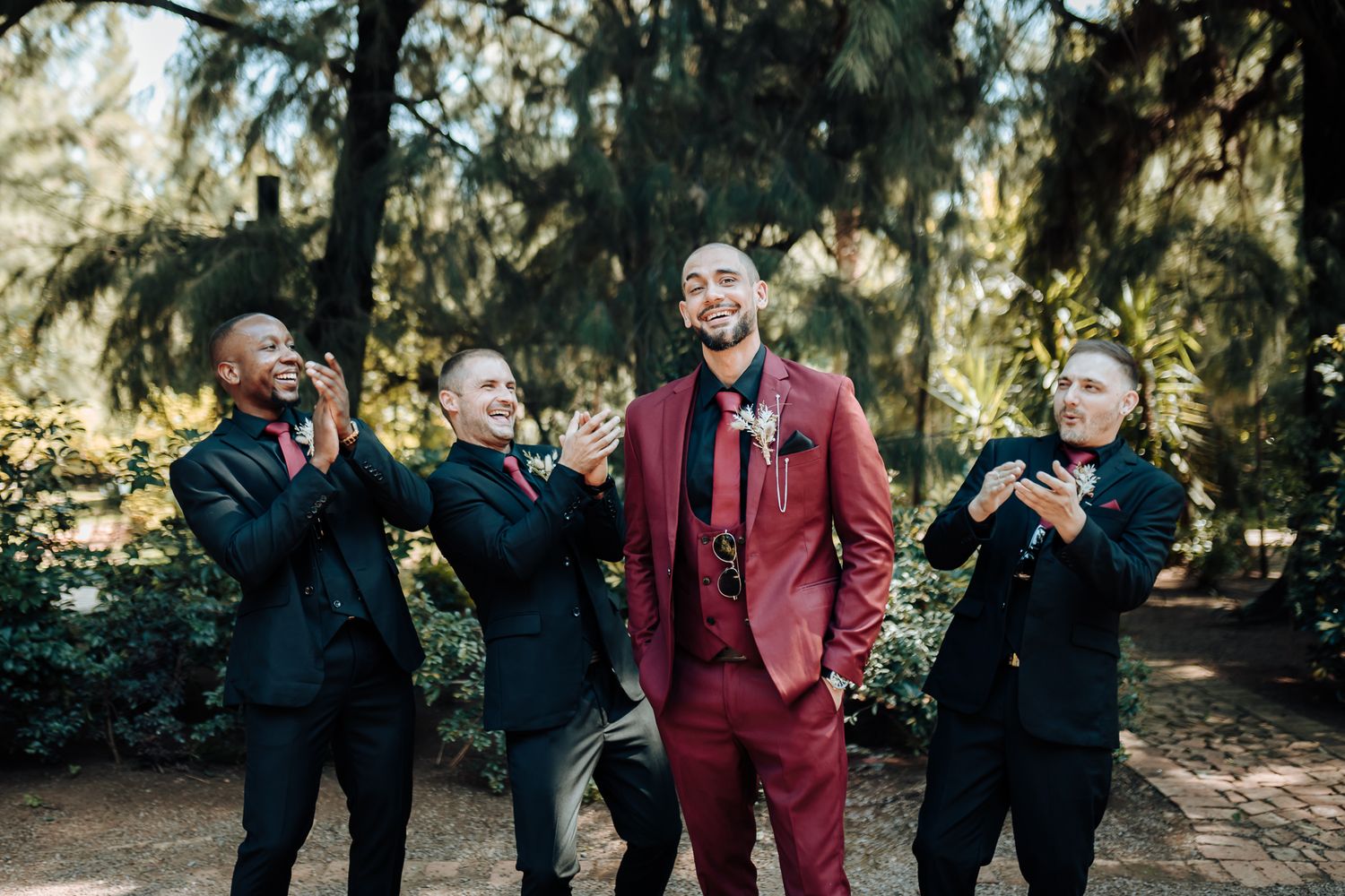 Wedding party laughing together in coordinated suits outdoors.