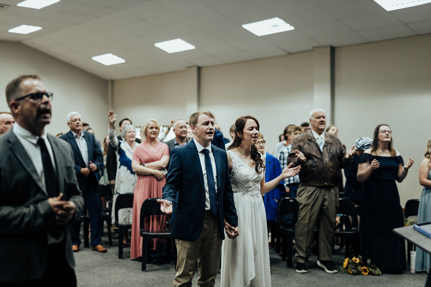 A group of wedding guests sing and worship together in an indoor venue.