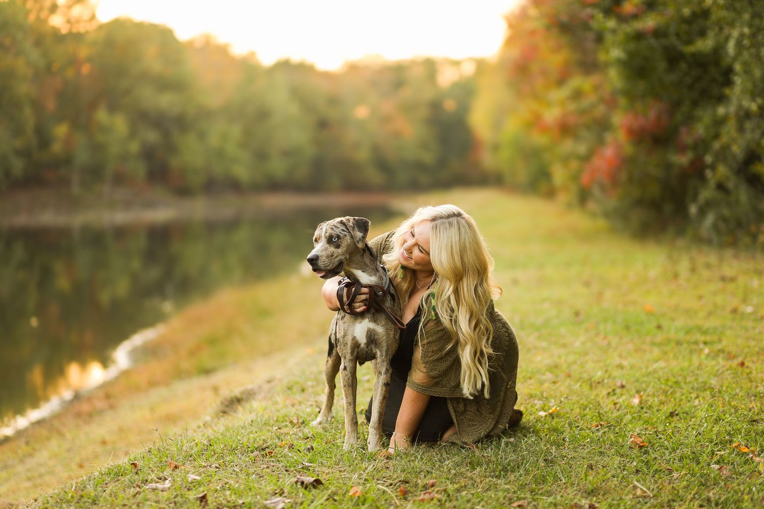 A person and their large gray dog pose together on a grassy riverbank during golden hour sunset.