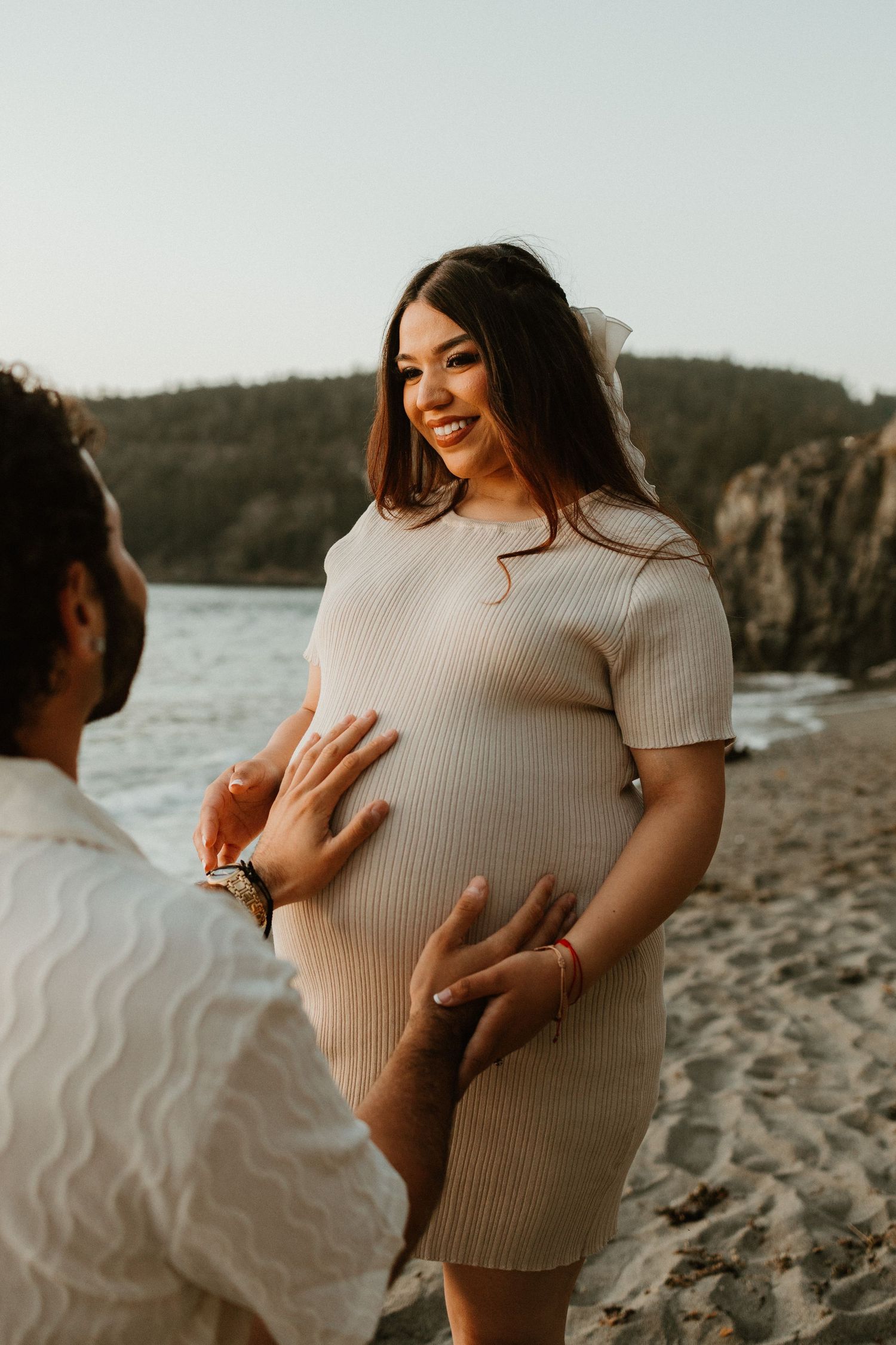 Sunset maternity photoshoot at a rocky beach with a loving couple in warm lighting.