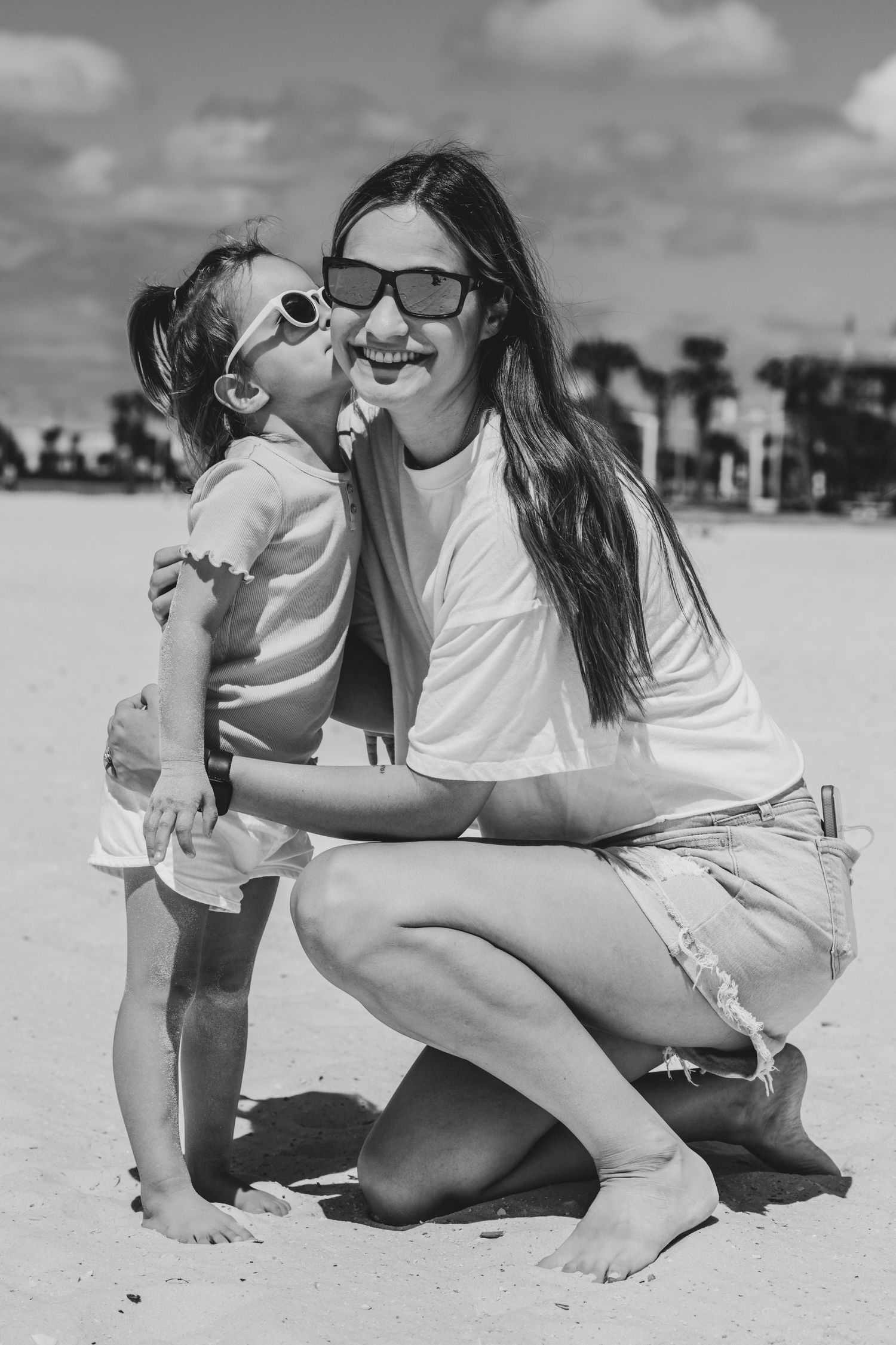 Black and white photo showing joyful moment between parent and child embracing on sunny beach.