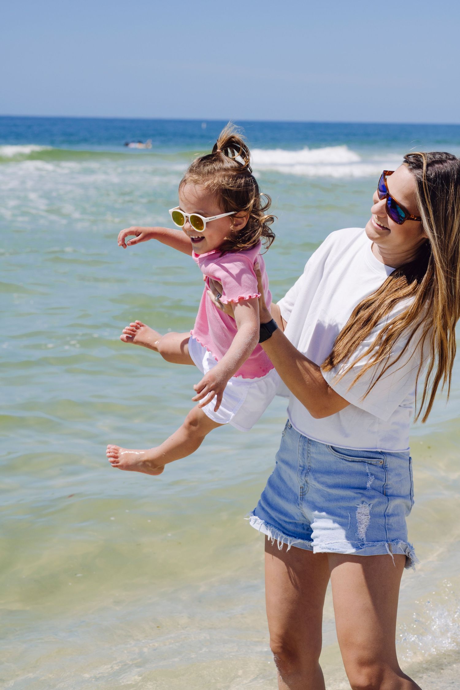 A playful scene at the beach shows a parent and child enjoying time together in the turquoise ocean waves.
