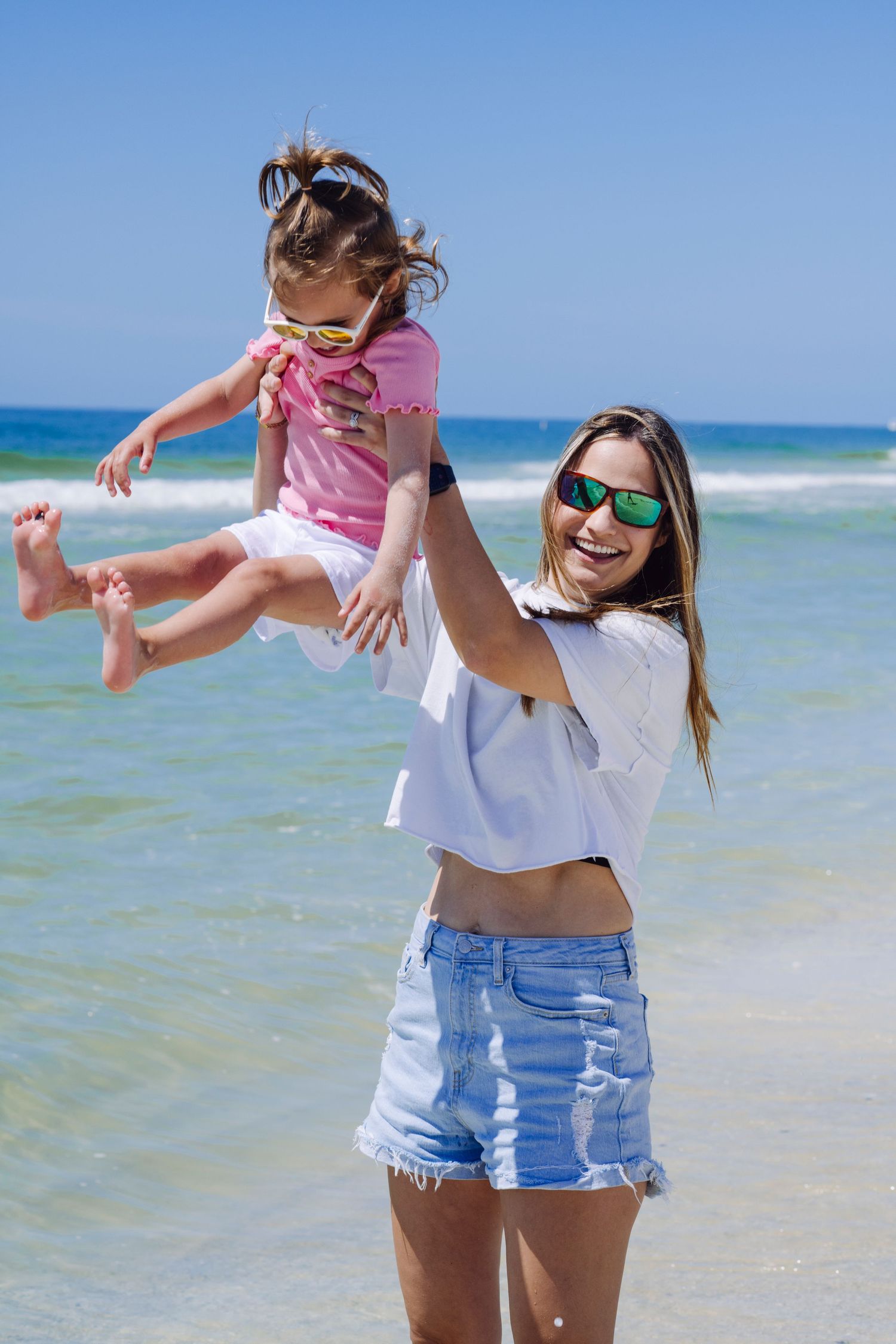 Two people enjoying a playful moment together by the beach with turquoise waters and blue skies in the background.