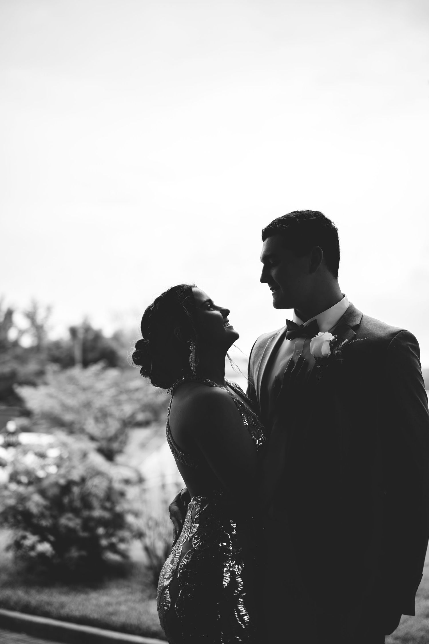 Black and white candid silhouette of a romantic couple laughing and embracing in an outdoor garden setting.