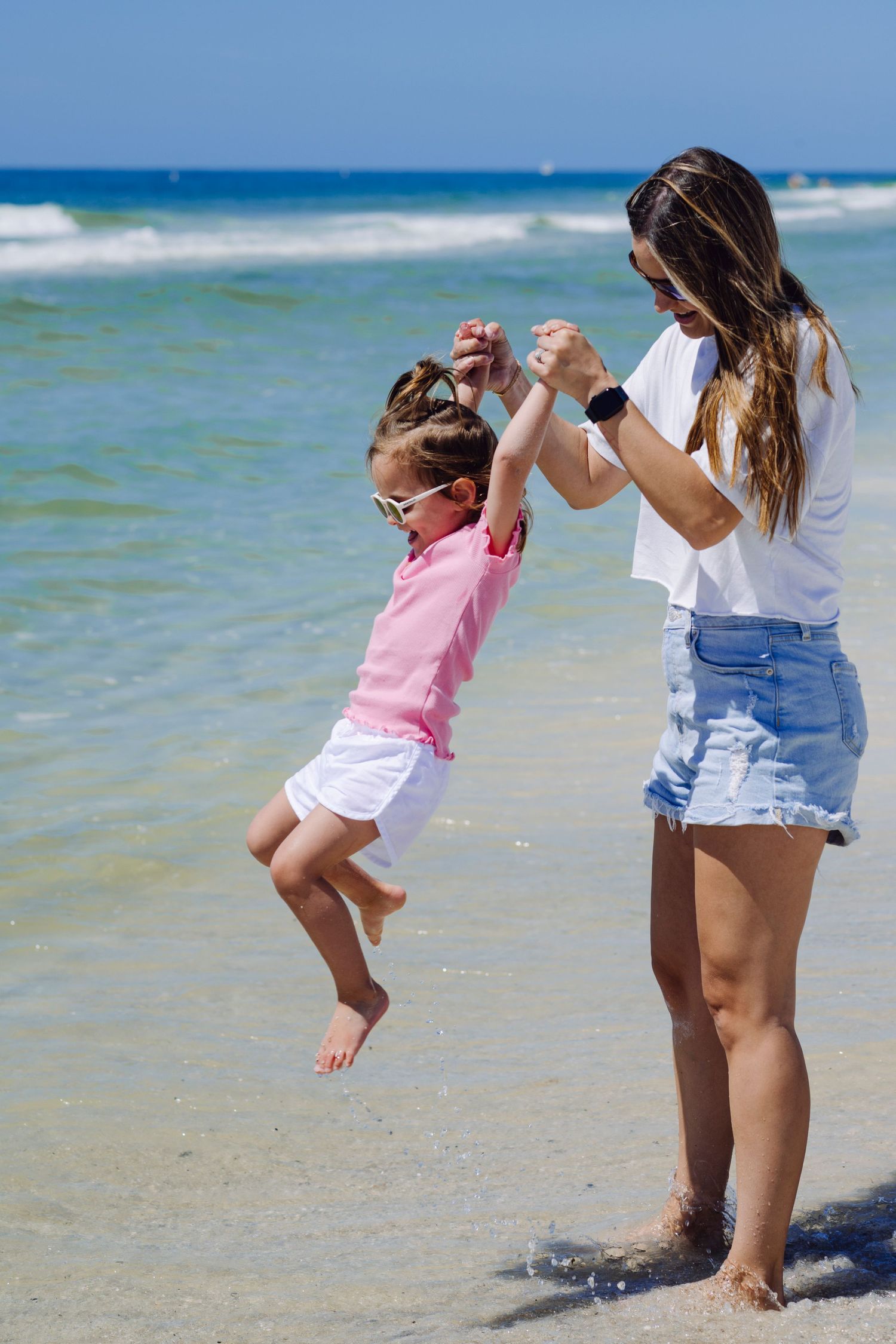 Two people enjoy a playful moment together at the beach with crystal blue waters and waves in the background.