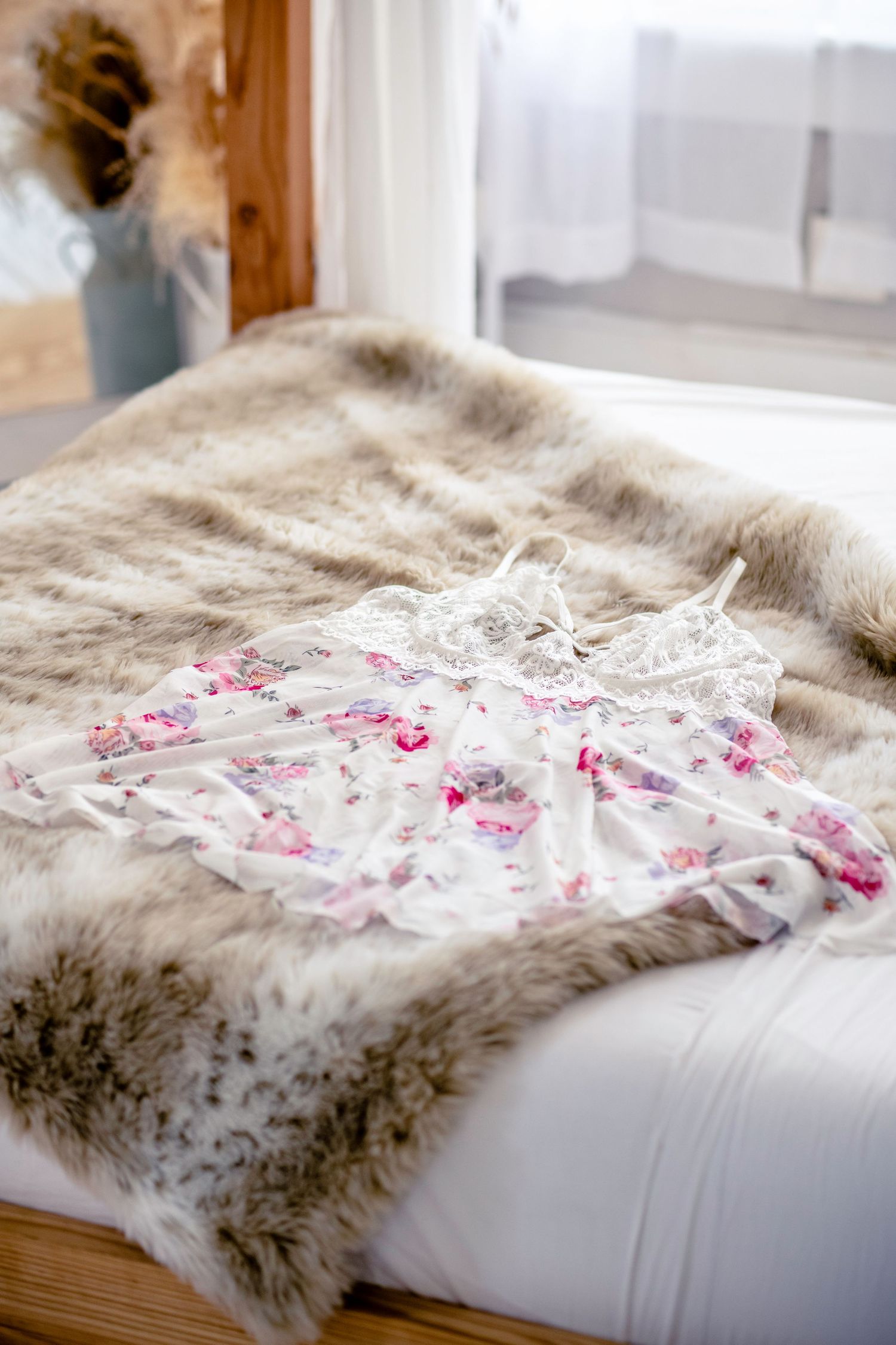 A delicate floral nightgown lies on a plush faux fur blanket in a boudoir studio near a bright window with soft natural lighting.