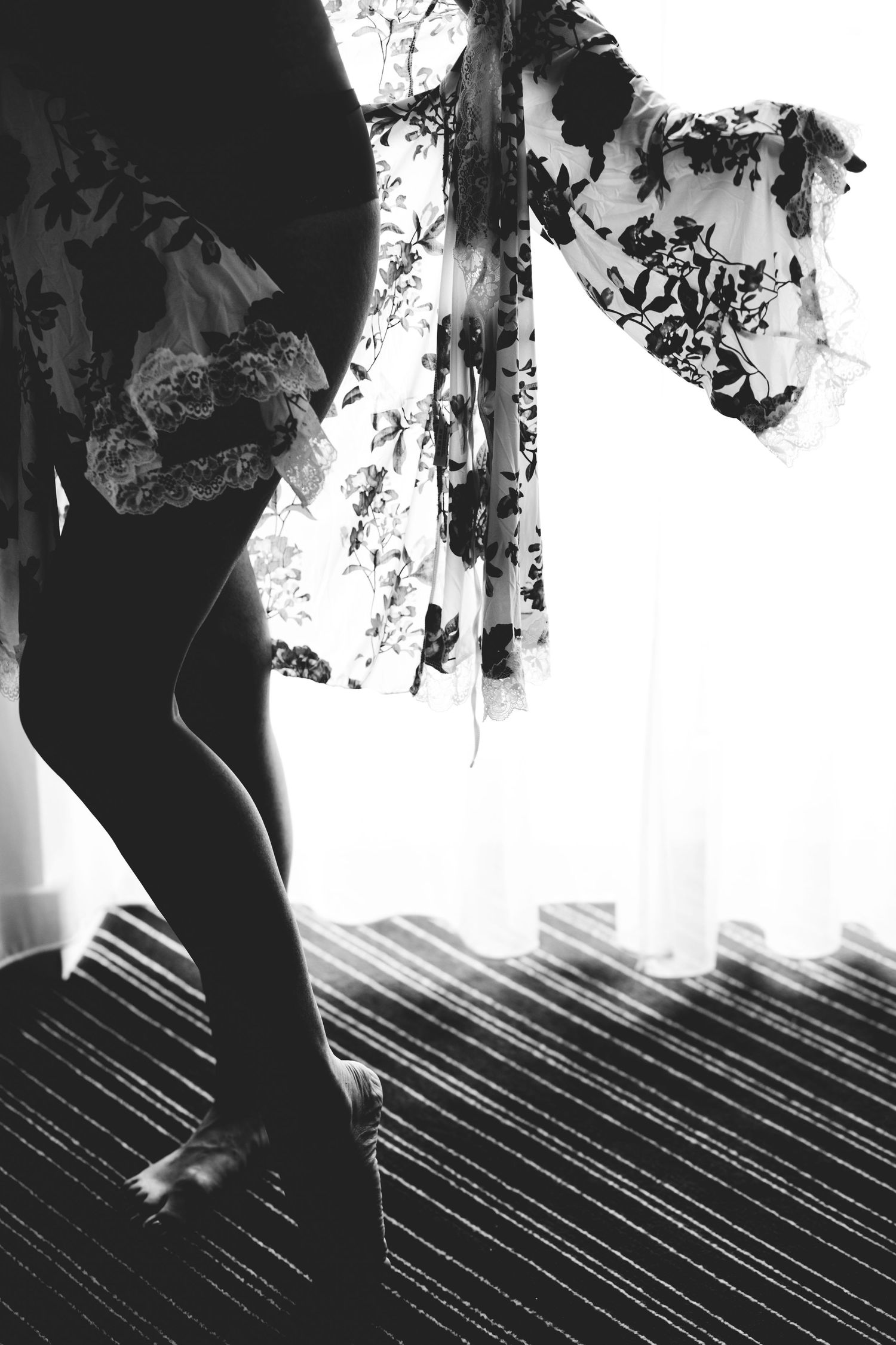 French Boudoir: black and white artistic photo showing a silhouette of legs in stockings against a backlit window with sheer curtains.