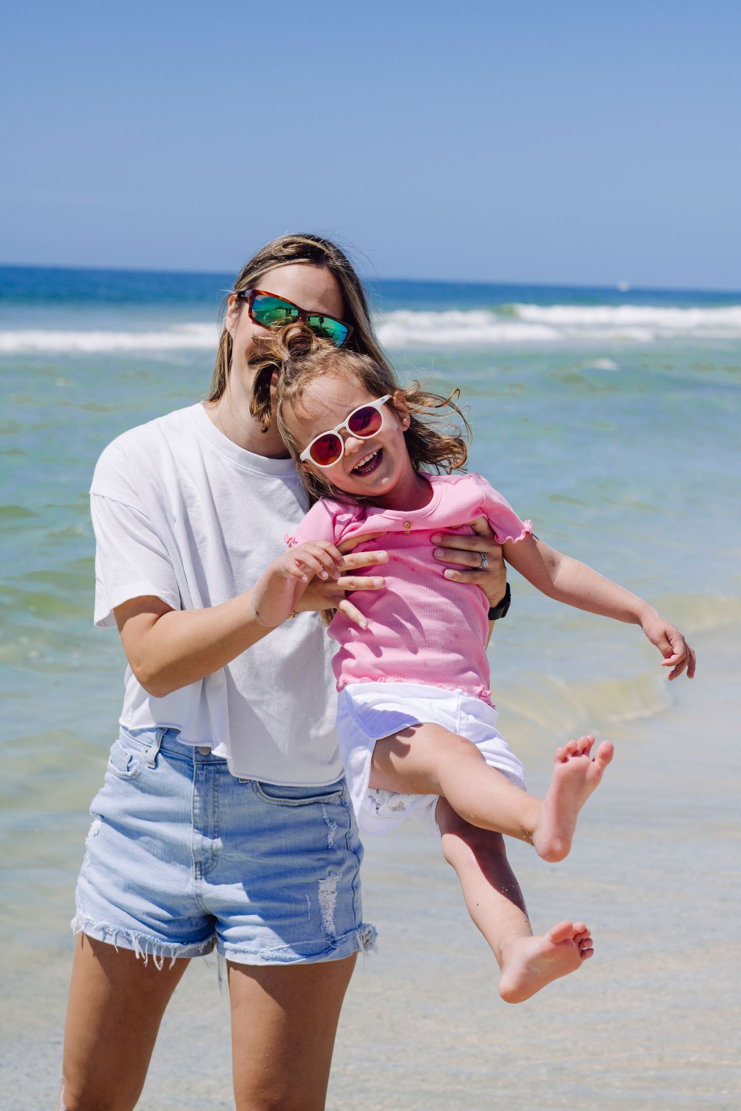 A parent and child playing together on a sunny beach with ocean waves in the background.