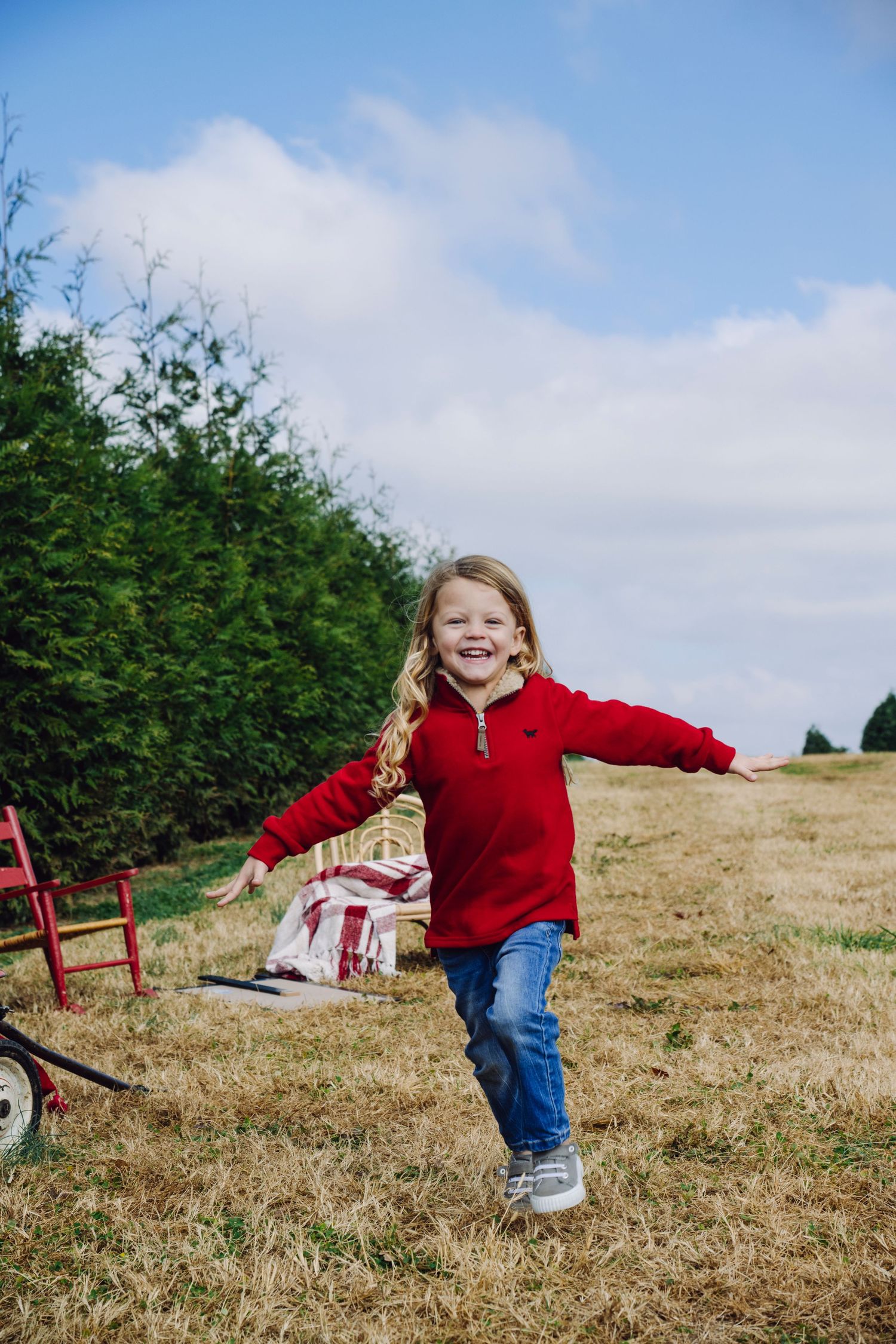 A child wearing a red sweater and jeans runs playfully through a grassy hillside field under blue skies in this Christmas lifestyle session.