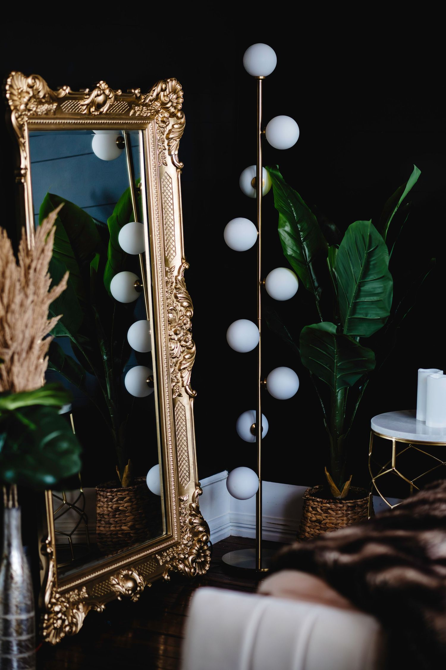 Luxurious boudoir studio with modern decor of ornate gold mirror, and tropical green plants against dark background.