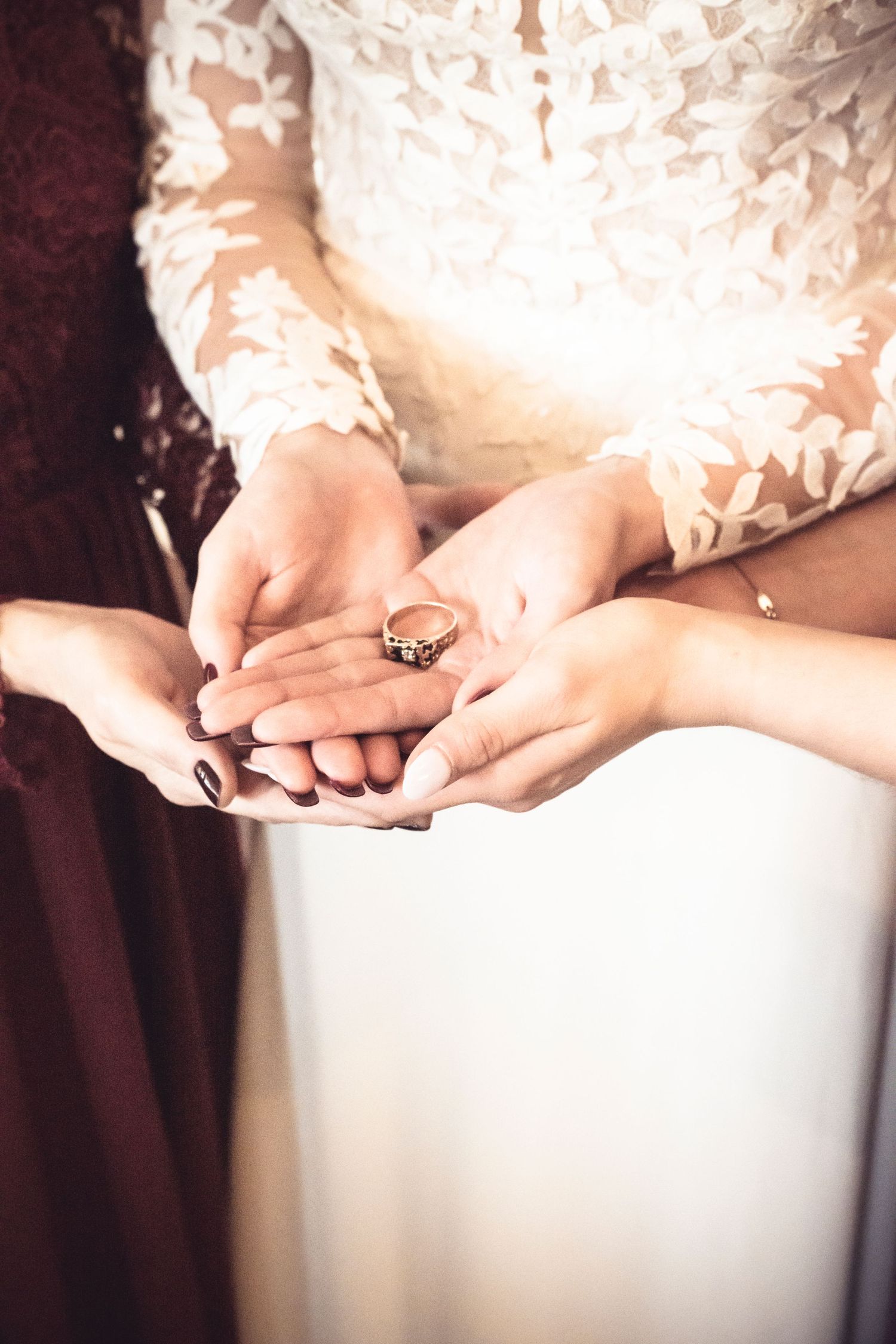 A close-up shot of hands holding a diamond engagement ring against lace fabric in soft lighting.