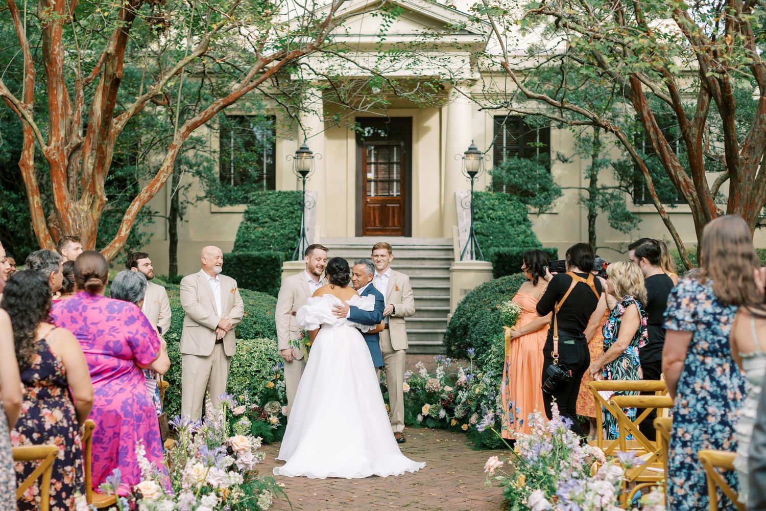 Wedding ceremony takes place outside a historic building with guests seated on both sides.