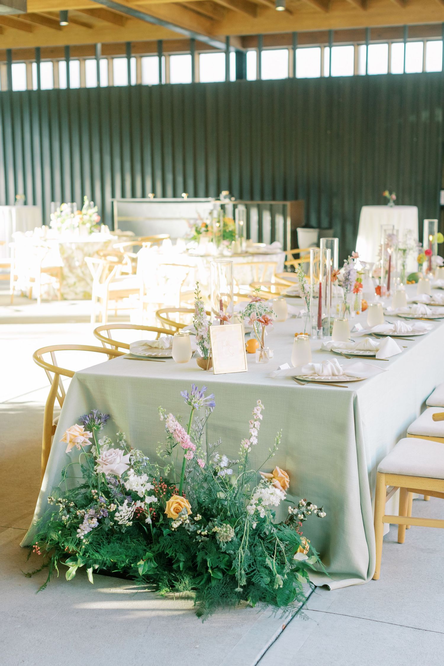 Wedding reception tables decorated with elegant floral runners and wooden chairs in an industrial-style venue.