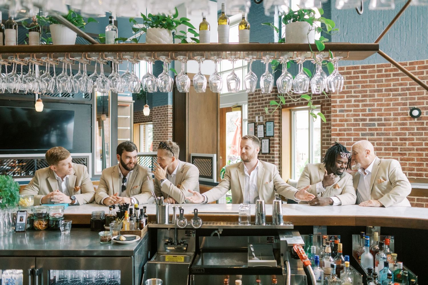 Professional bartenders in white uniforms prepare drinks at an elegant bar counter with glassware and spirits displayed.