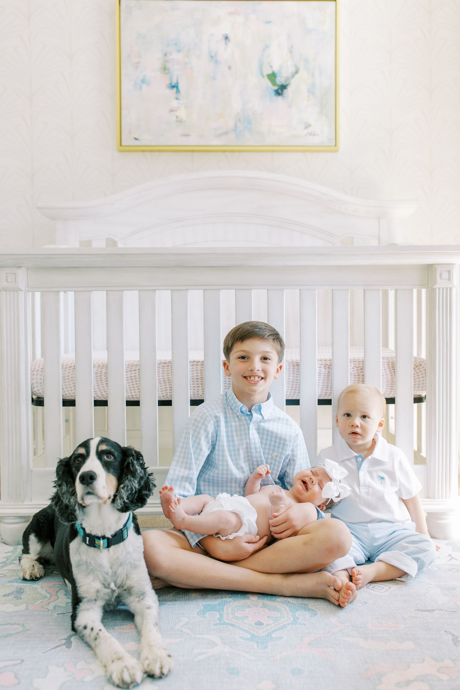 A nursery scene with a white crib, abstract art, and a dog sitting next to children on the floor.
