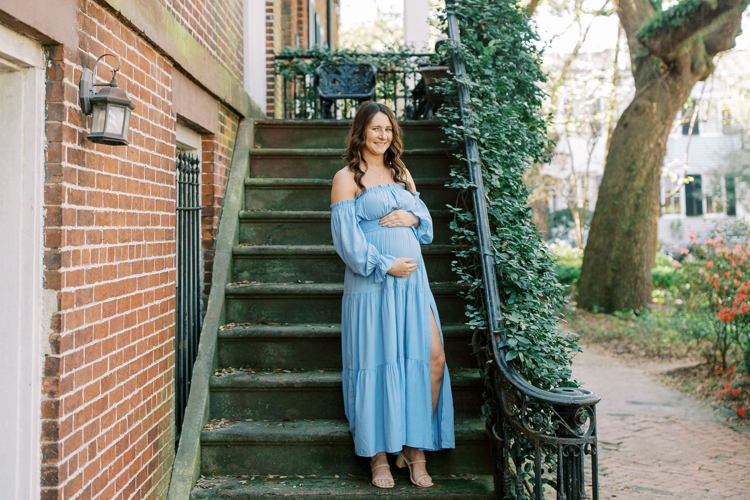 Someone wearing a long light blue dress stands on brick exterior stairs surrounded by ivy and greenery.